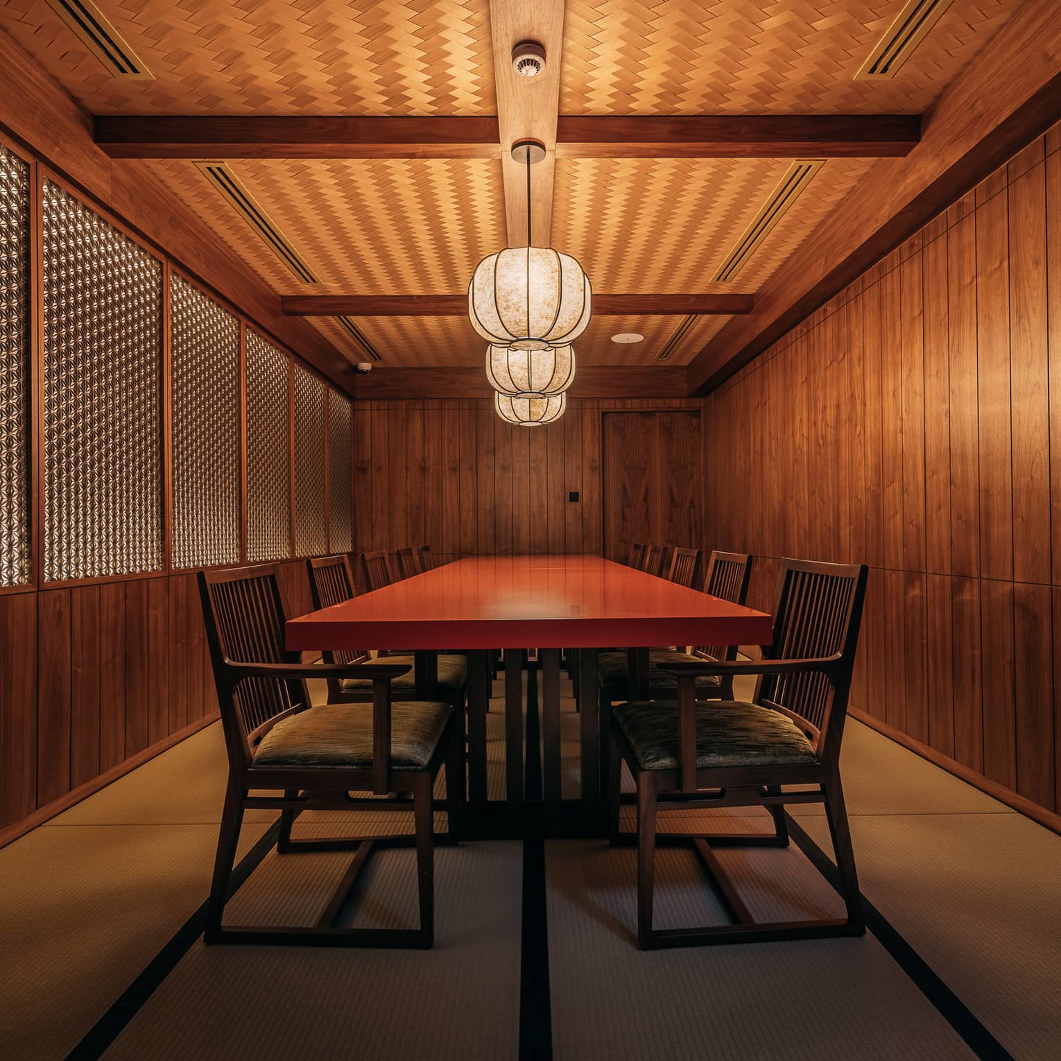 Private dining room with Japanese-style wood panelled walls and a red rectangular table in the centre sert beneath three paper lanterns