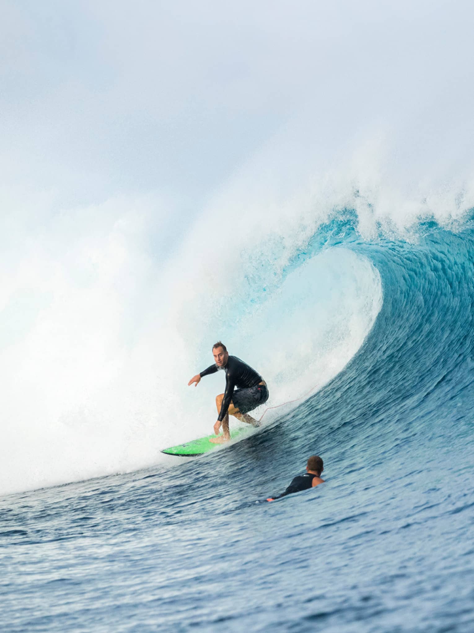 Surfer rides surfboard on large wave, two surfers swimming in water