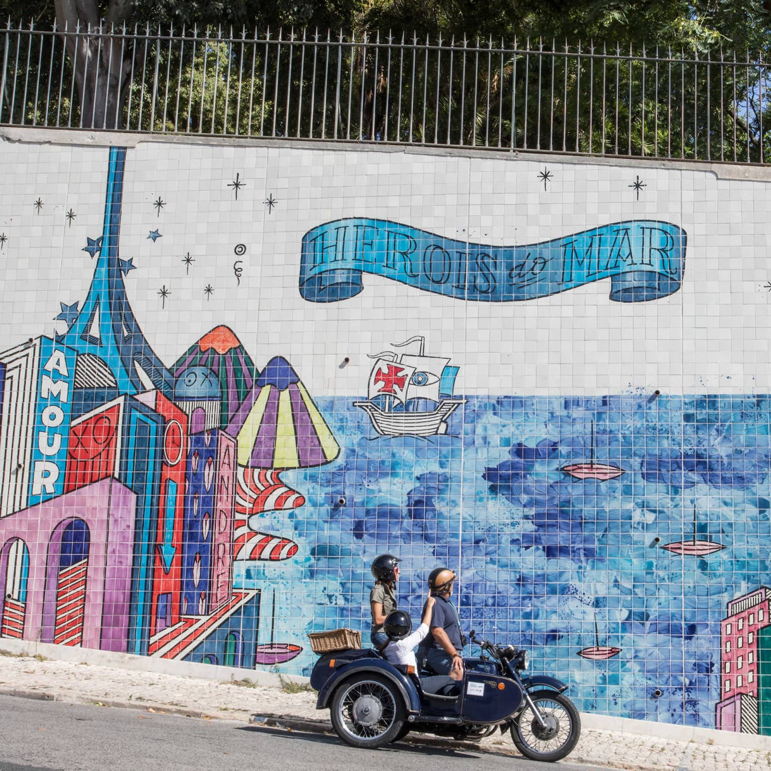 Two adults and a child stop their motorcycle to look at a city mural made of tiles