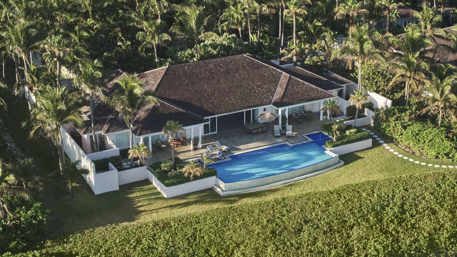 Aerial view of large Four Seasons Ocean Club villa bungalow, pool and lawns behind greenery, sand beach