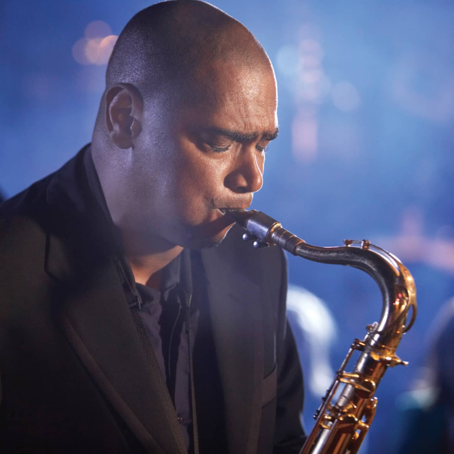 A close up of a man with his eyes closed, playing a saxaphone at a Jazz club in Ten Trinity