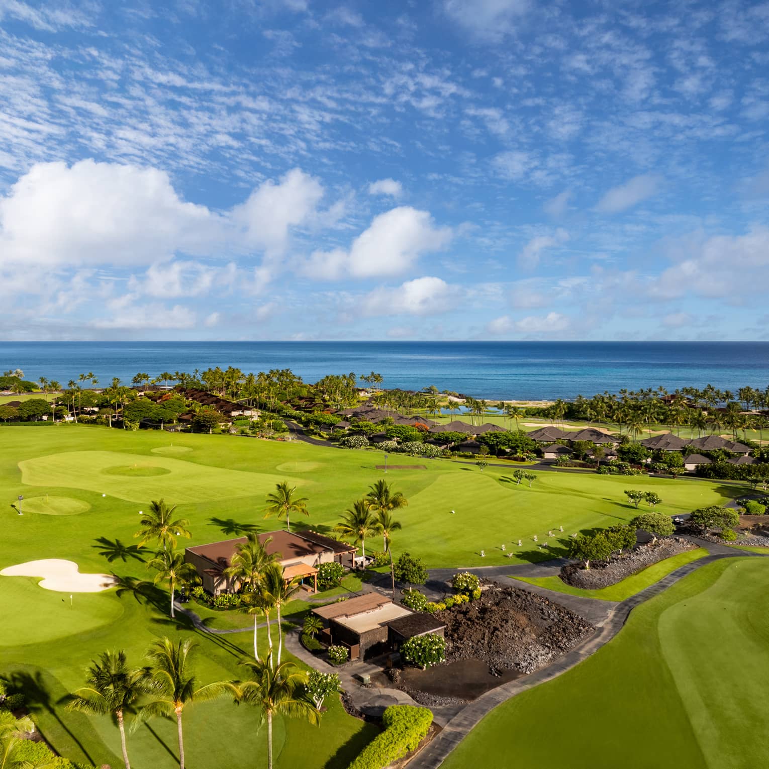 Aeriel view of a lush green golf course with natural lava formations and the ocean in the background.