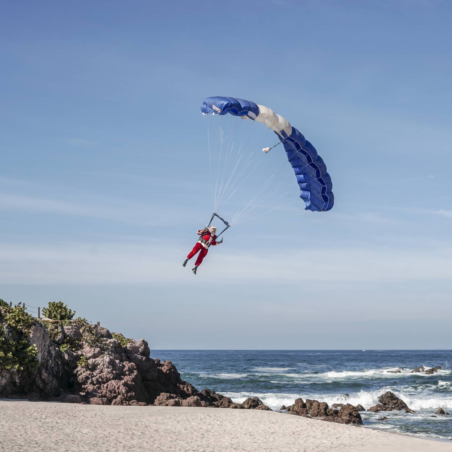 A man dressed in a Santa outfit in a parachute landing on the beach.