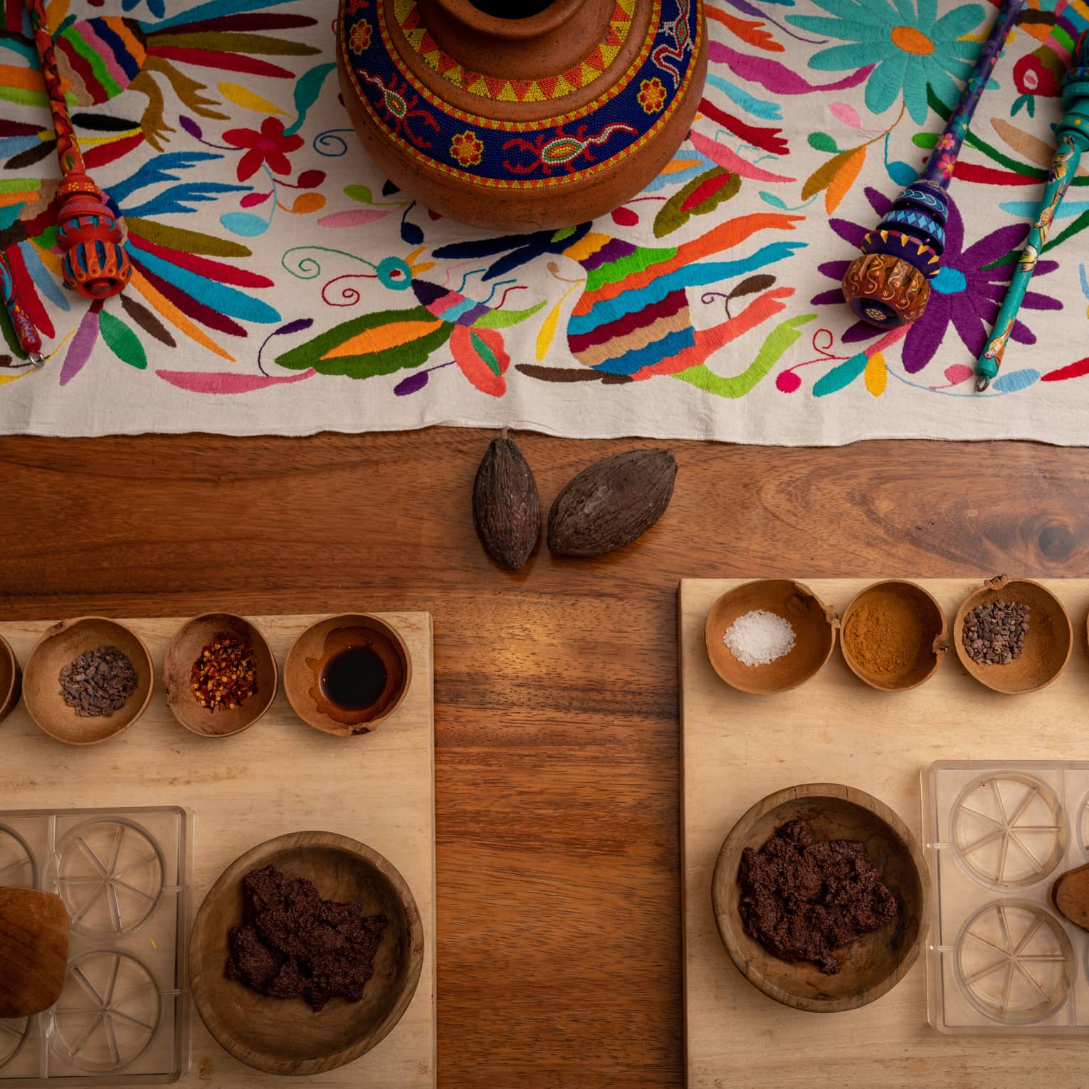 On a wooden surface, a bright tapestry, platters, bowls containing various ingredients, clear moulds and mixing tools.