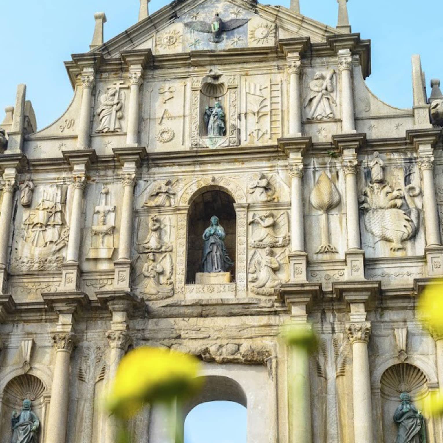 An ornate facade with archways at bottom, lined with thin towers and columns, intricate carvings and shelves holding statues.