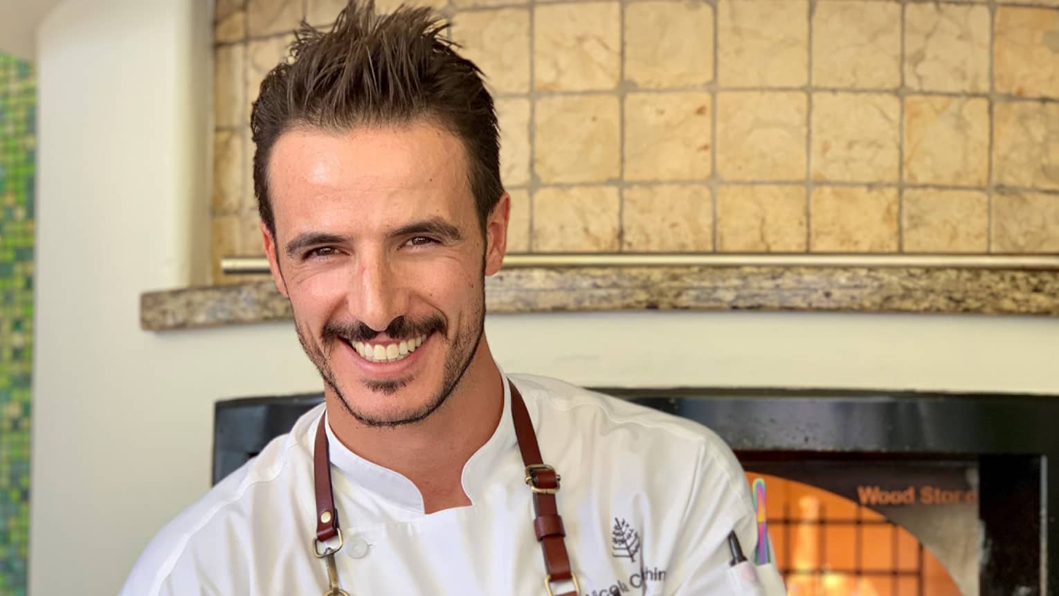 Chef Nicola Cavicchini smiles holding a pizza