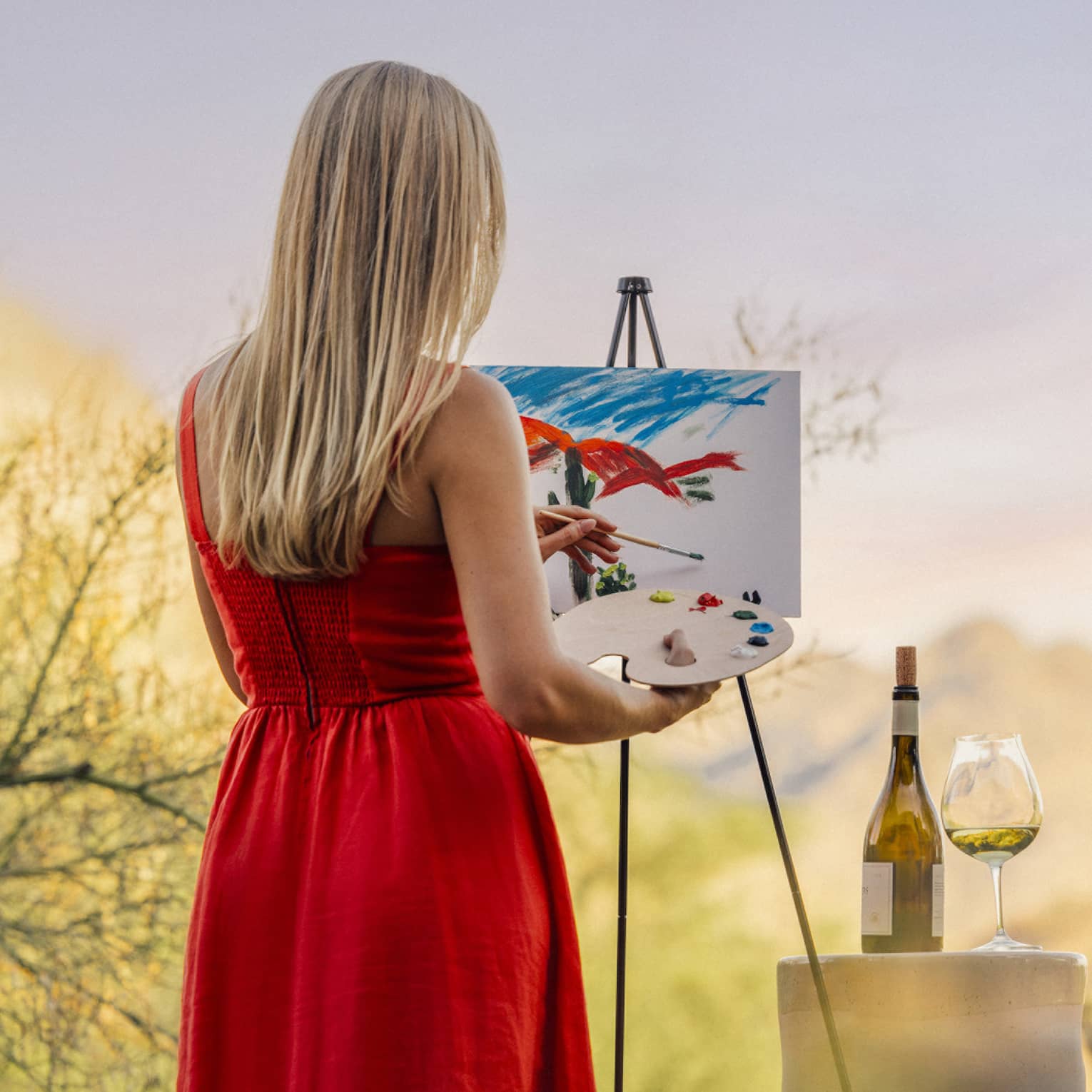 Person wearing a red dress and painting with a wine glass beside them.
