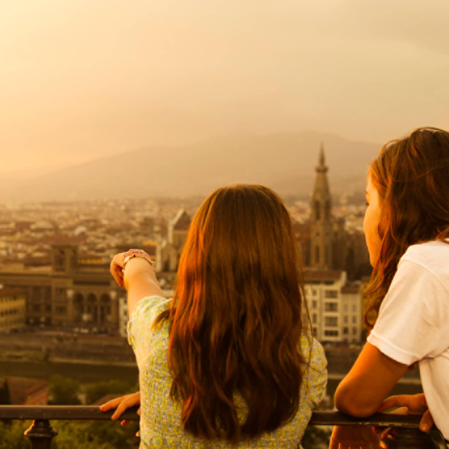Back of two young girls looking out over Florence skyline, rooftops, Duomo at sunset