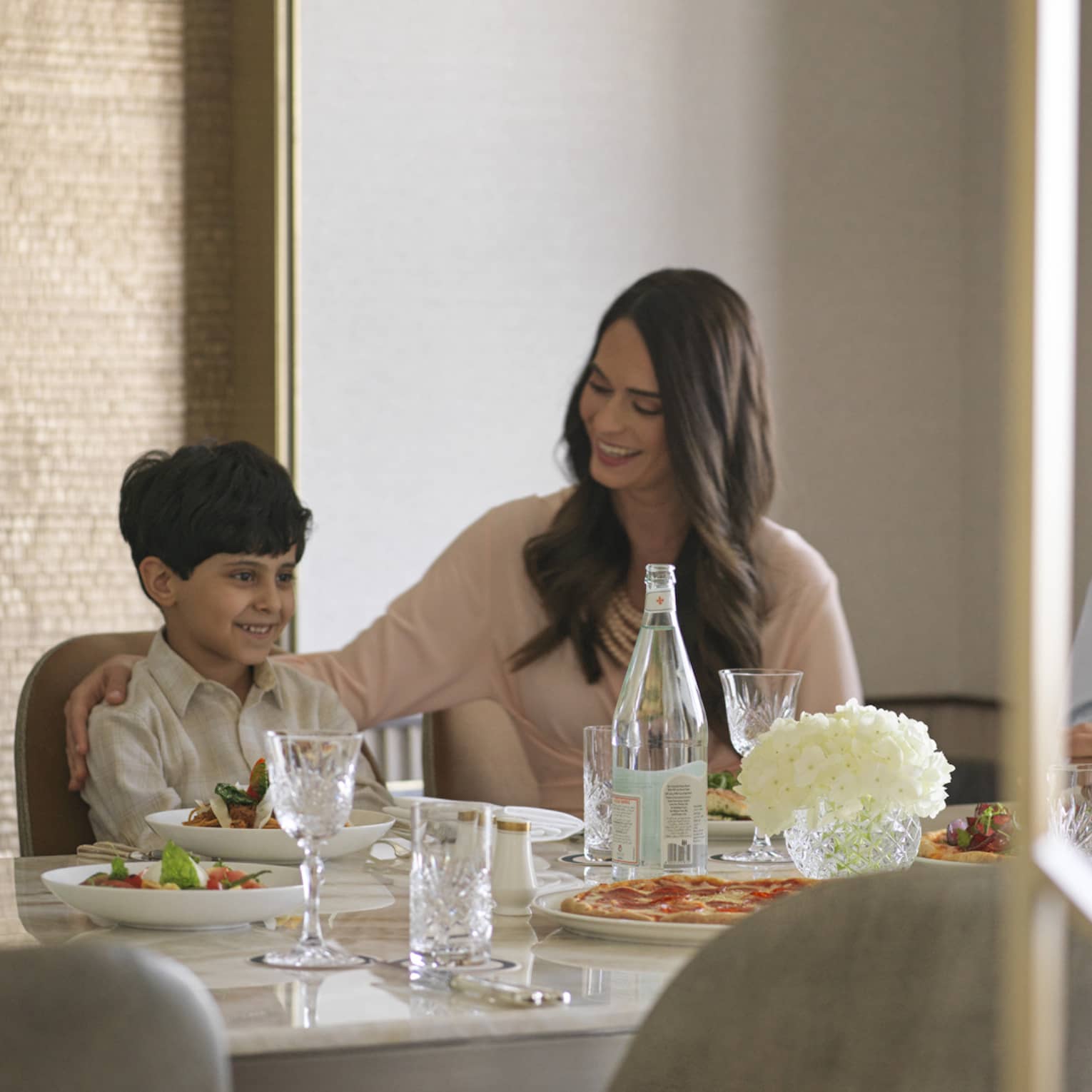 A view from the doorway of a smiling family sitting around a nicely set table with an assortment of food placed before them.