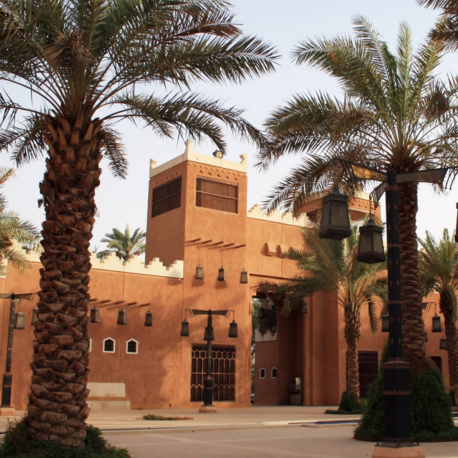 Sunny exterior of sandstone building and large palm trees with lanterns hanging from branches
