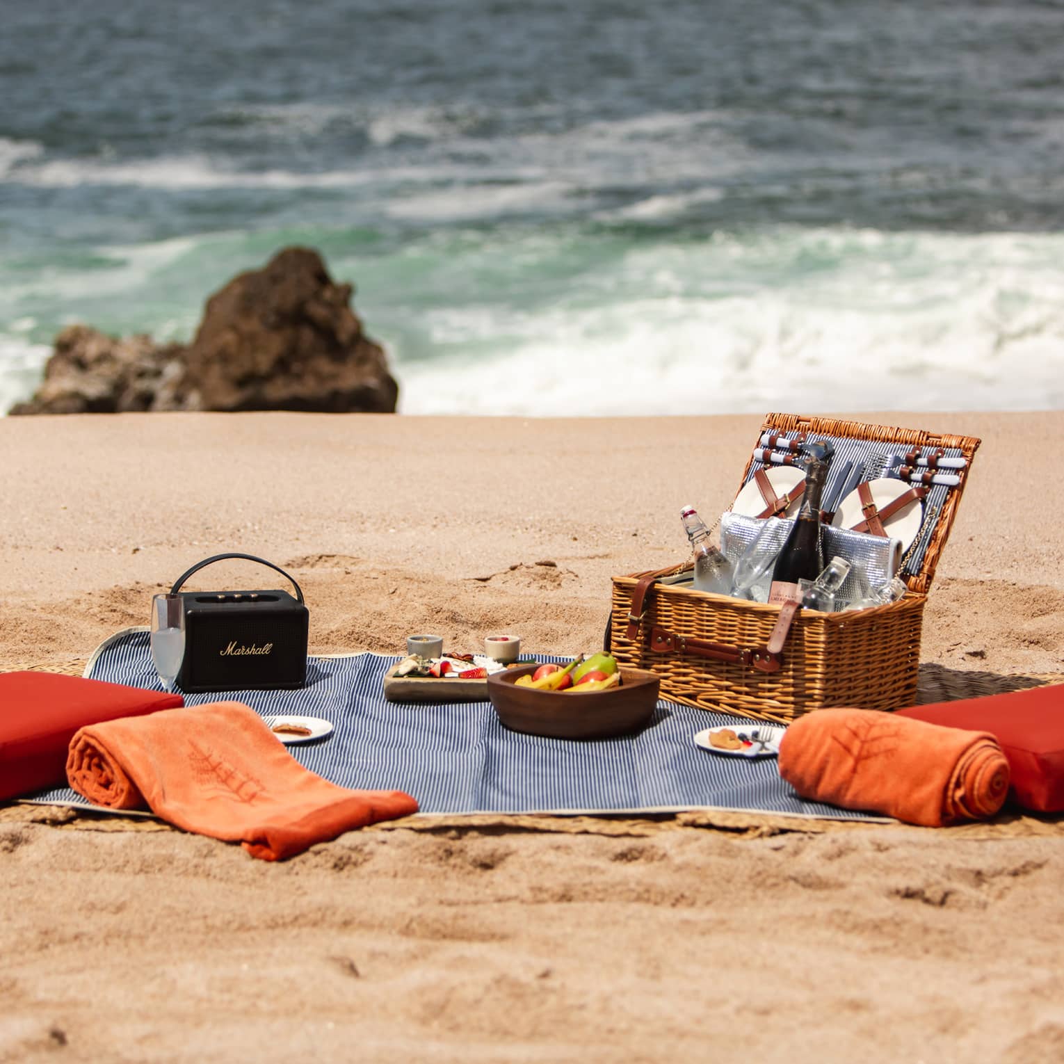 A picnic basket with cushions and a blanket on a beach.