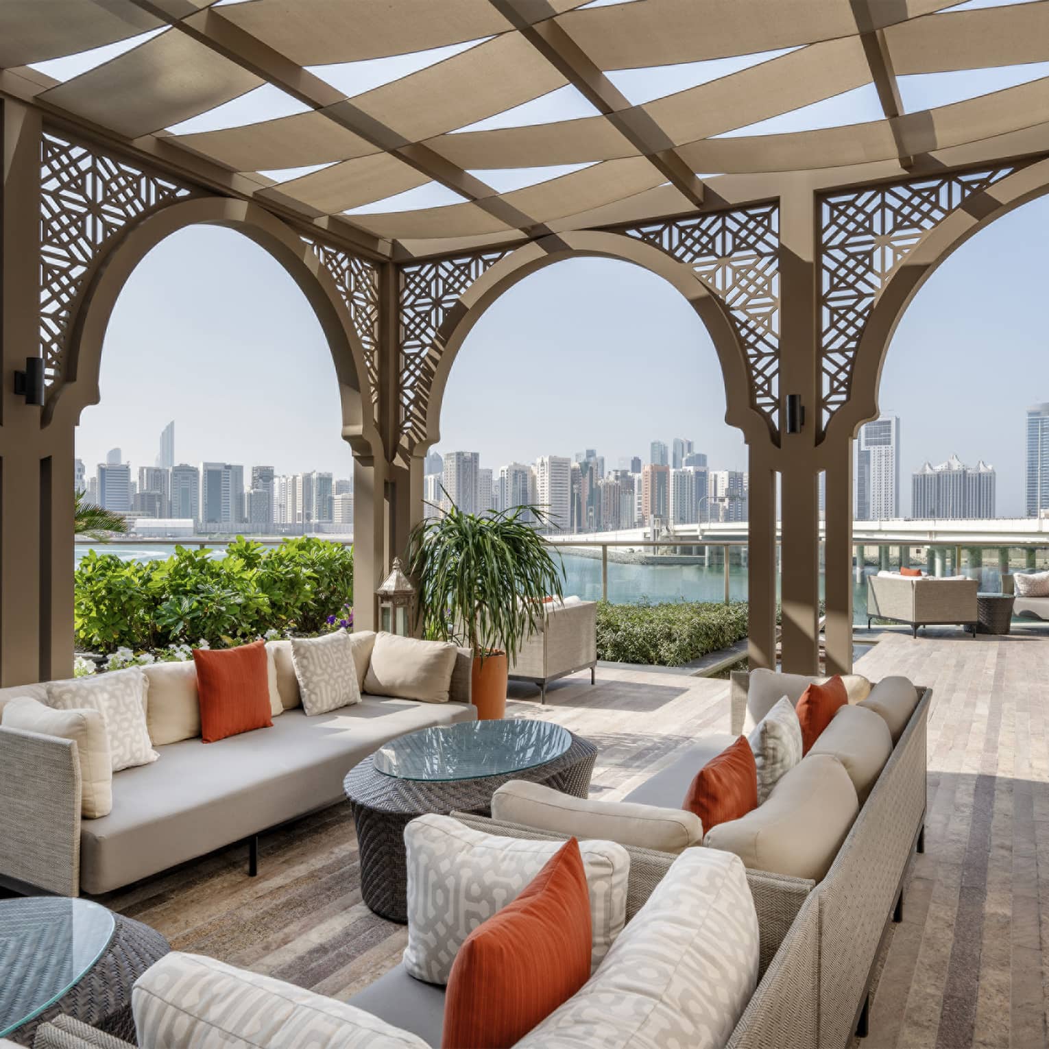 Large open-air terrace furnished with sofas and coffee tables, featuring view of a city skyline in the distance