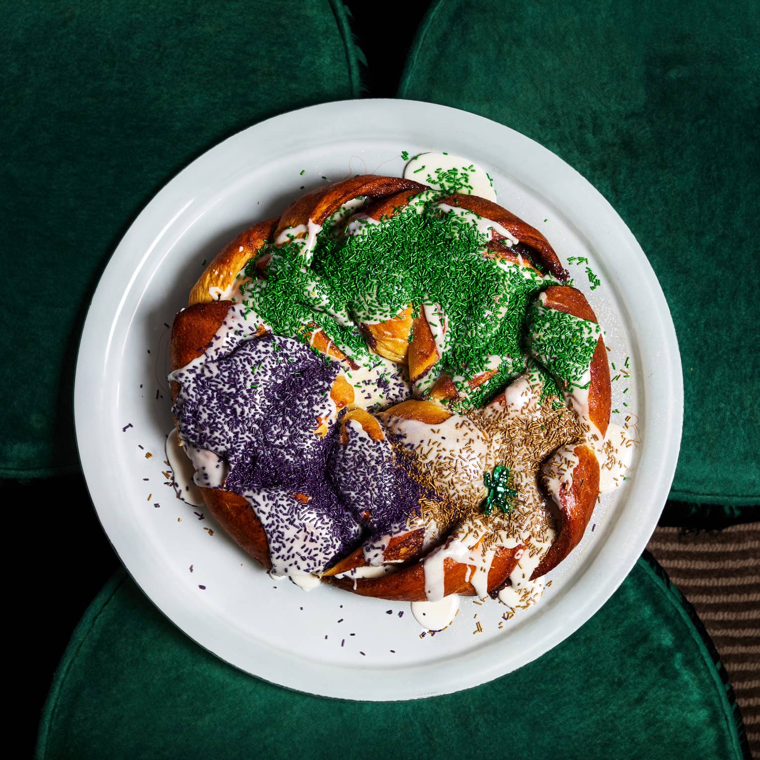 A round white plate holding pieces of king cake with white icing and green, purple and golden sugar topping