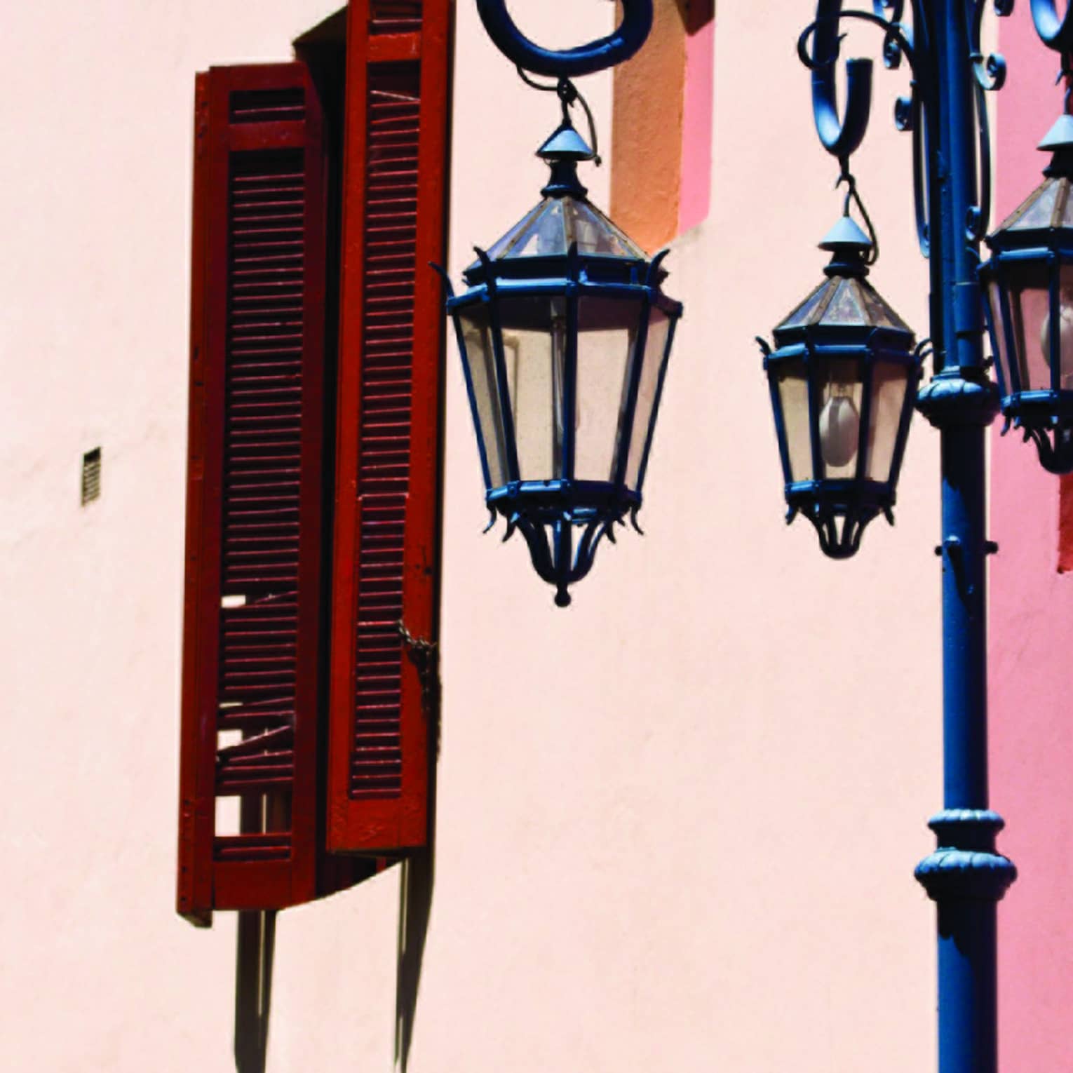 An ornate blue streetlight sits in front of a building painted in bands of rich watercolours and set with dark wood shutters.