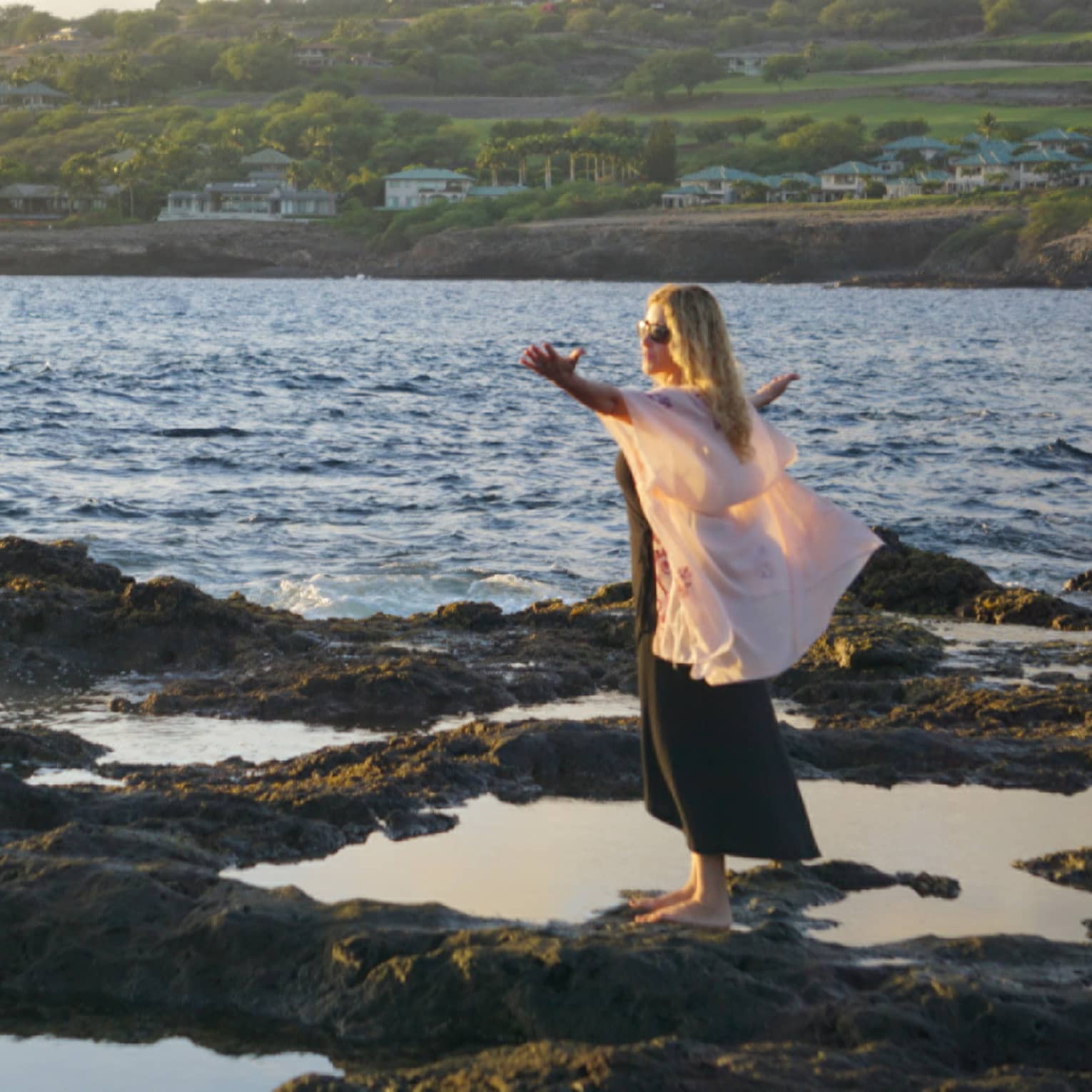 A woman meditates at edge of ocean on lava rock