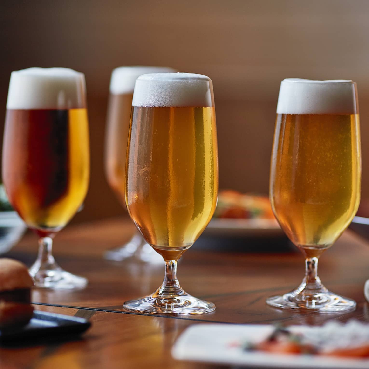 Four tall beer glasses filled with beer on a table with cheese, crackers and appetizers