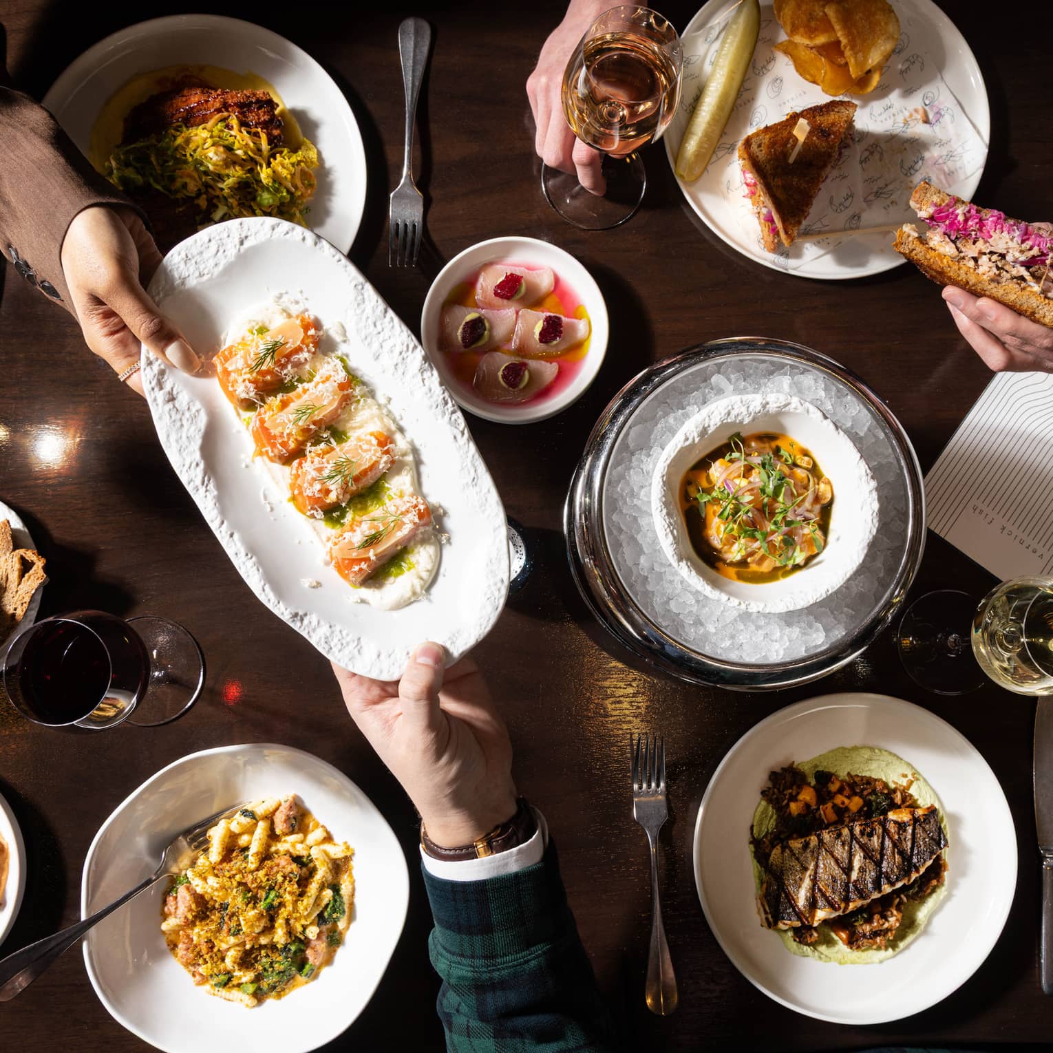 A dark wooden table topped with various colourful culinary dishes and glasses of wine