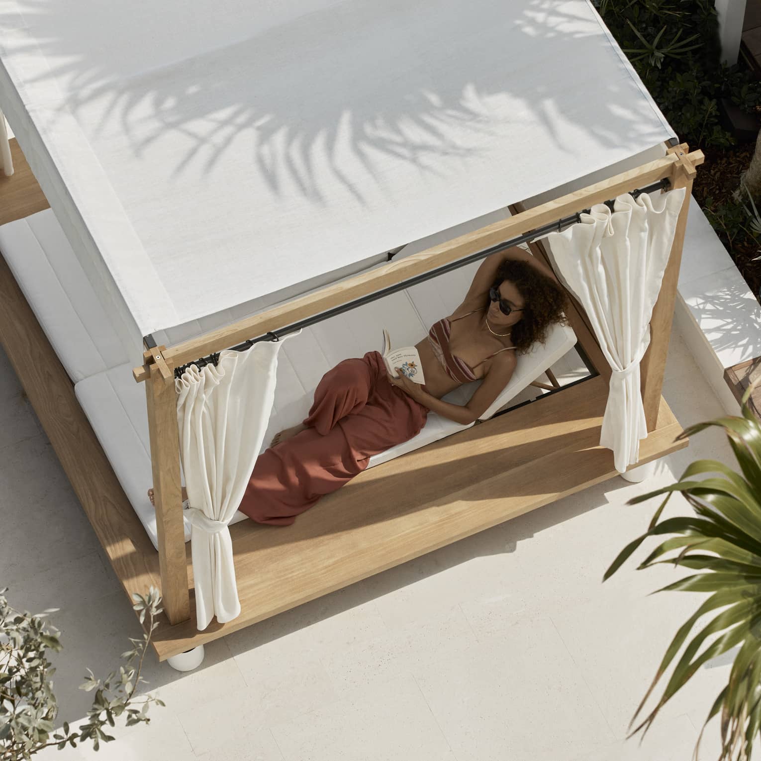 Aerial view of woman lounging in a covered poolside daybed