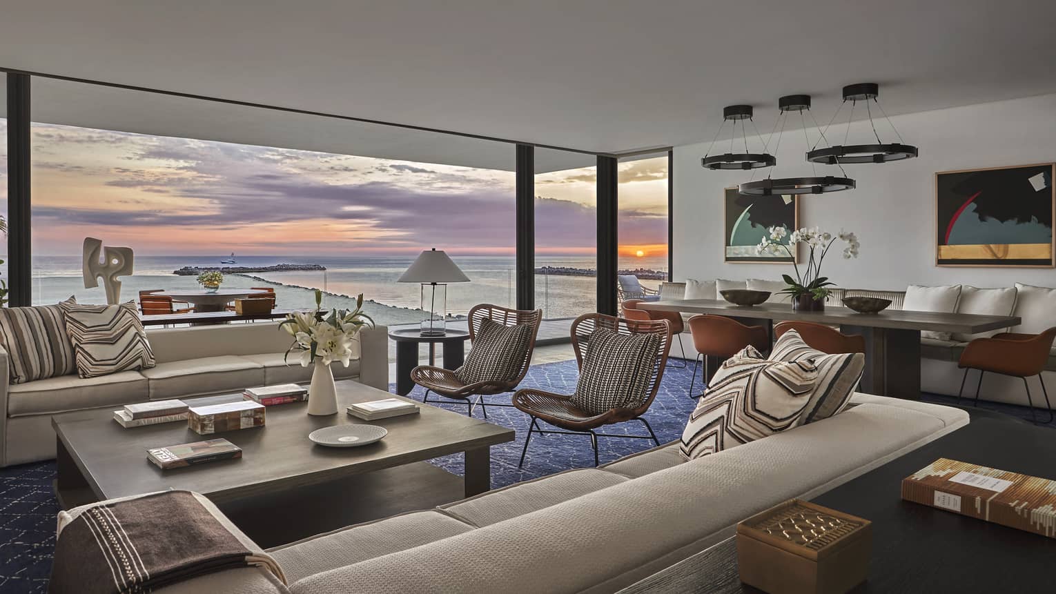 Hotel suite's living and dining area with sunrise view over ocean, through large sliding doors