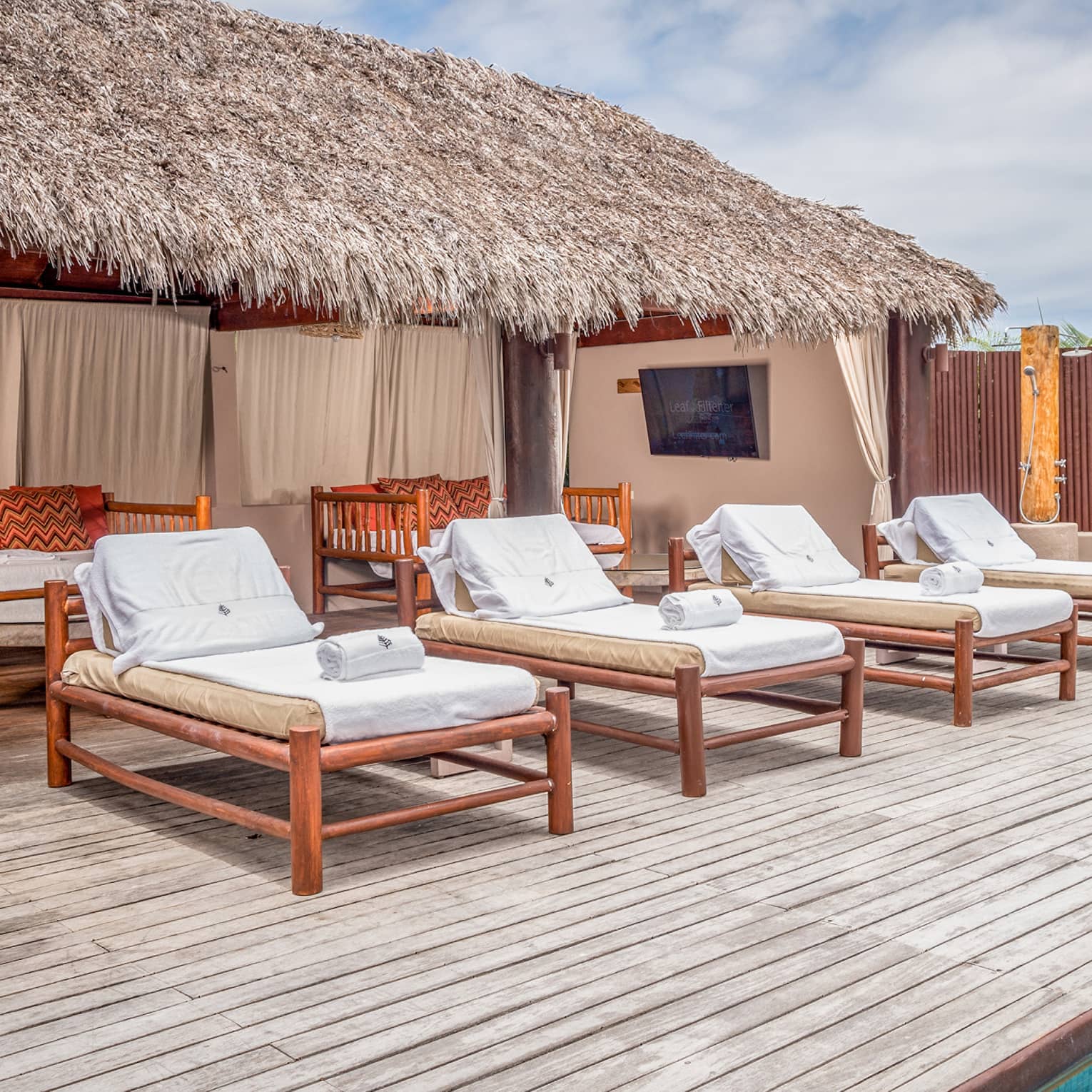 Pool cabana with four cushioned sun lounge chairs and wooden deck