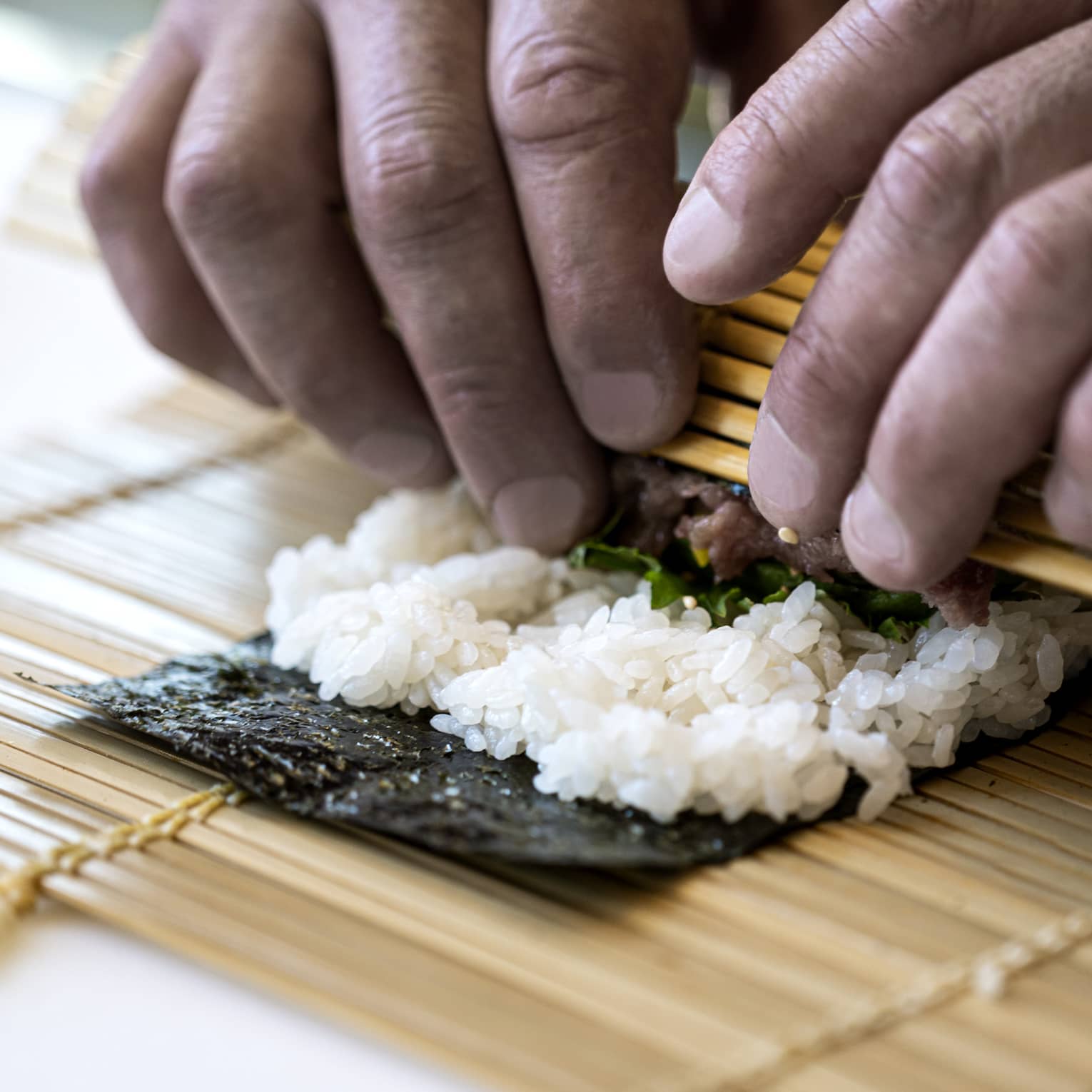 A four seasons chef rolls sushi with a bamboo mat