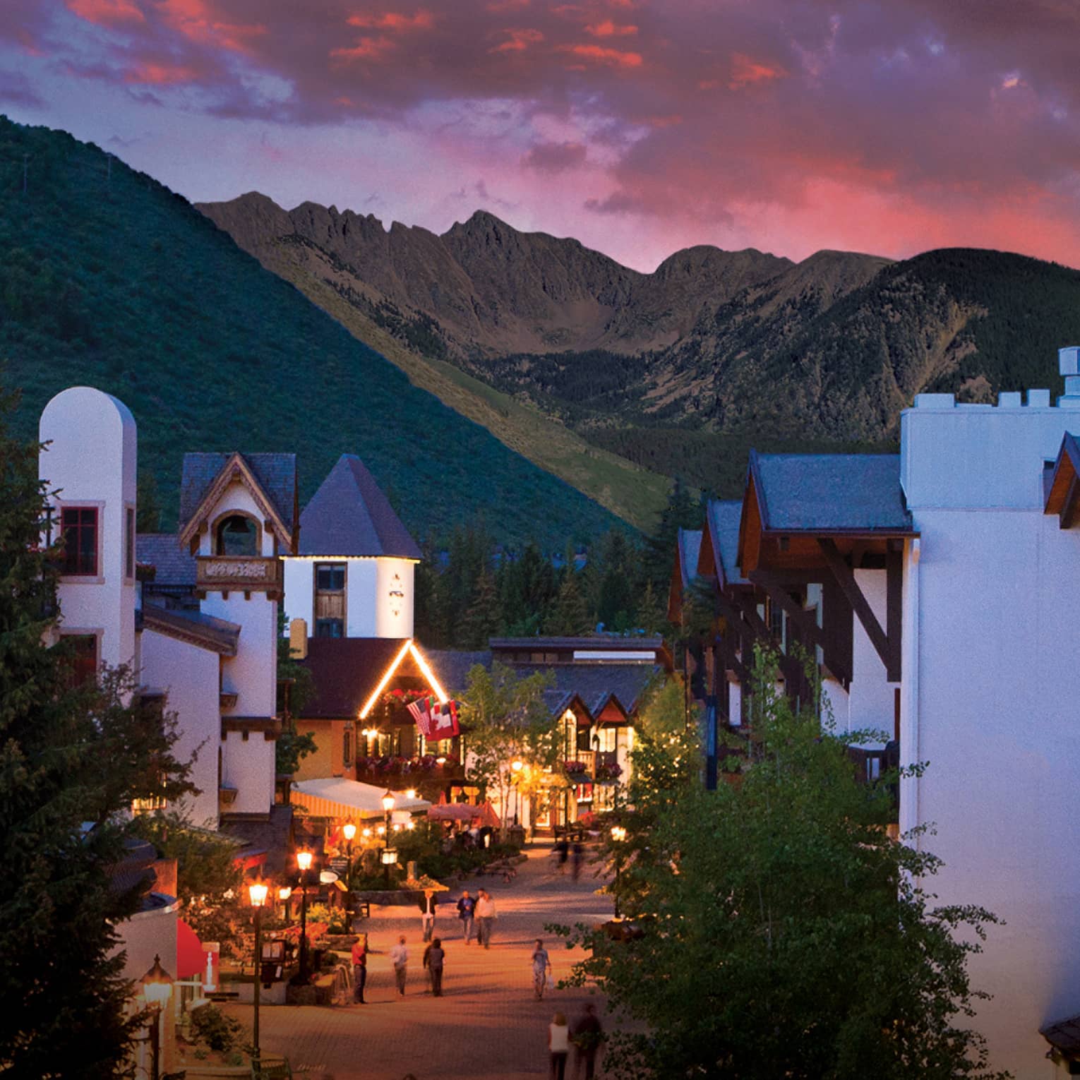 A sunset over a small village like city center with white buildings and mountains in the distance.