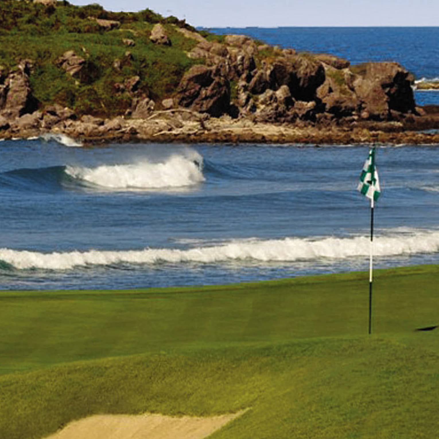 Bahia Golf Course flag on green beside rolling ocean tide, large rock