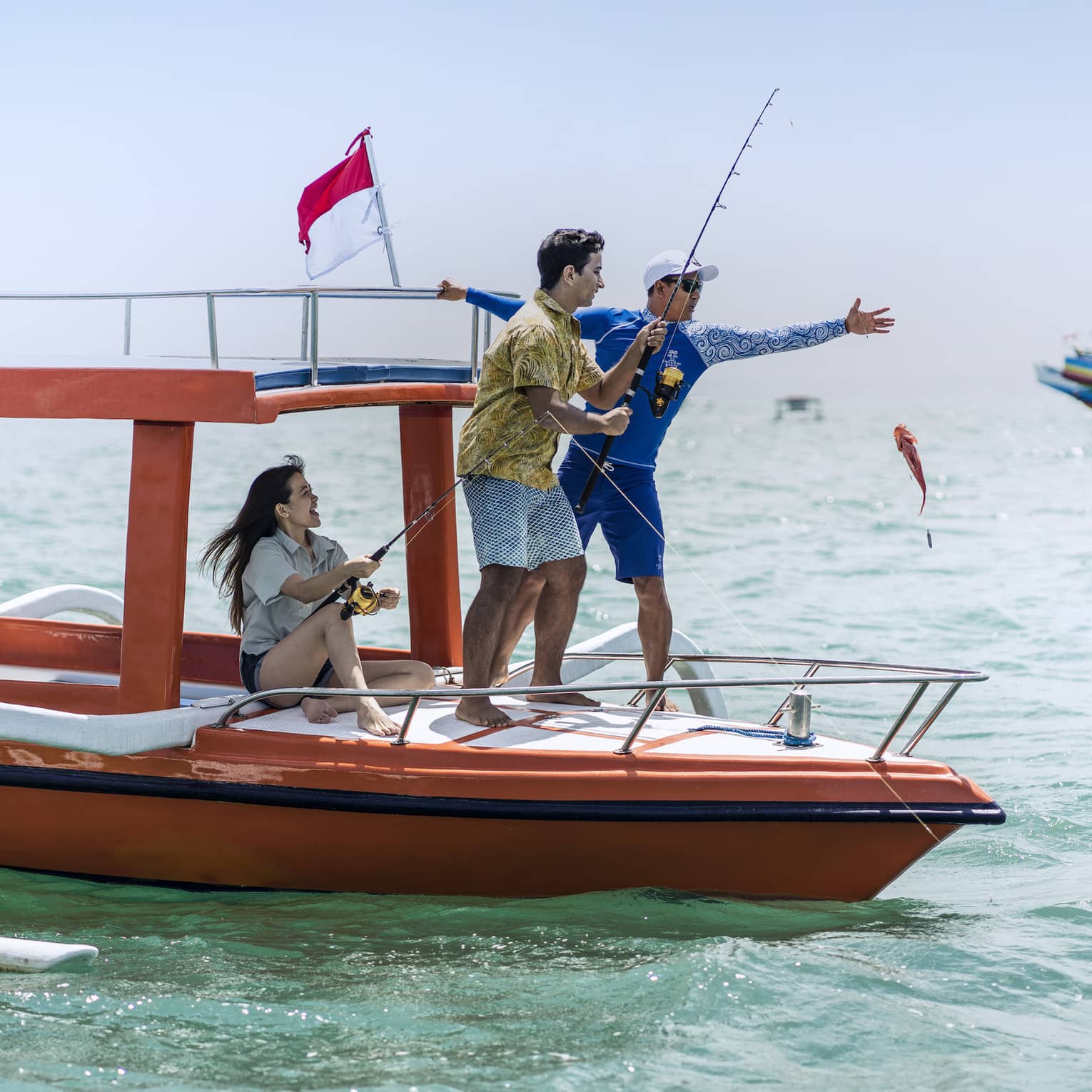 Tour guide teaches two guests to fish on a traditional jukung fishing boat on the open ocean