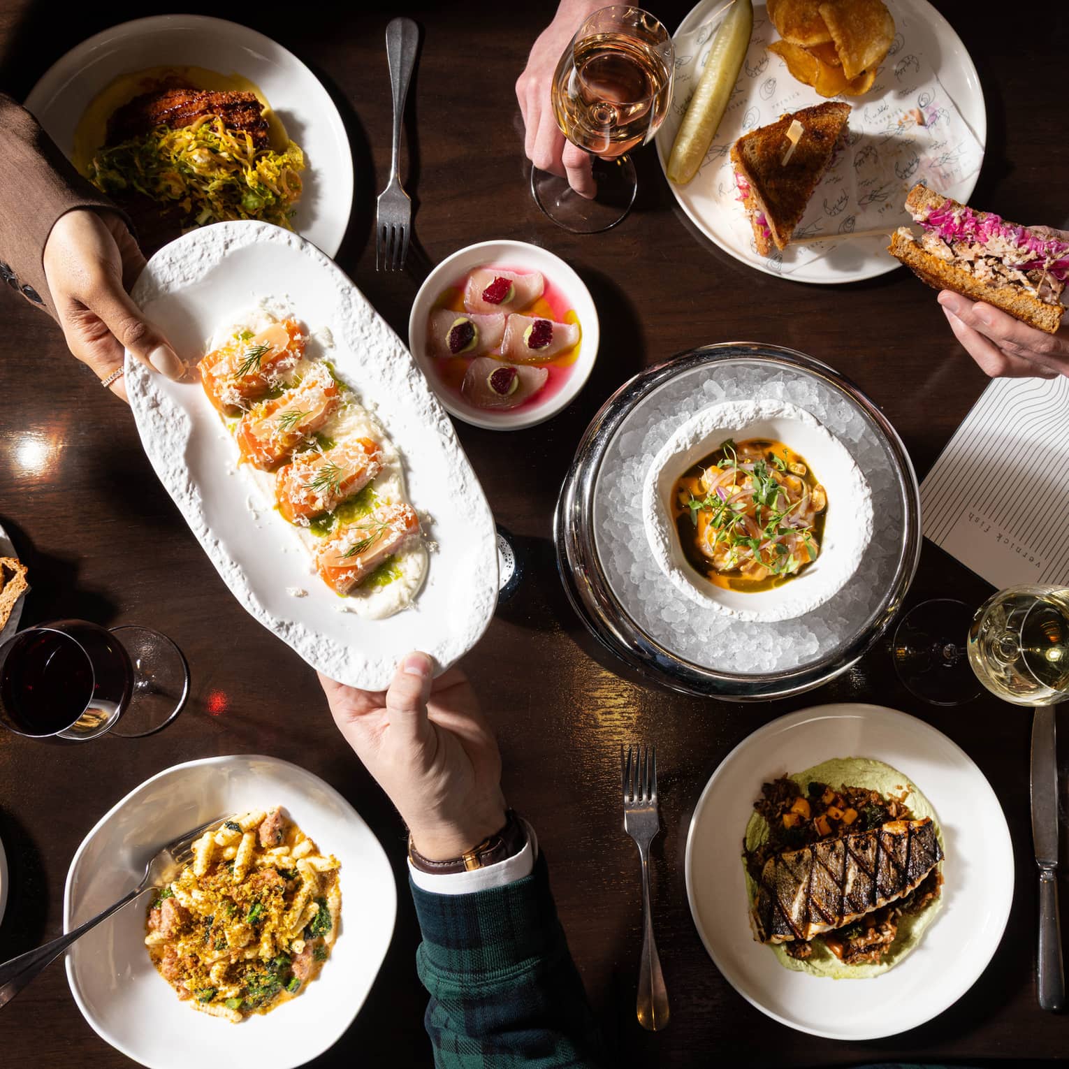 A dark wooden table topped with various colourful culinary dishes and glasses of wine