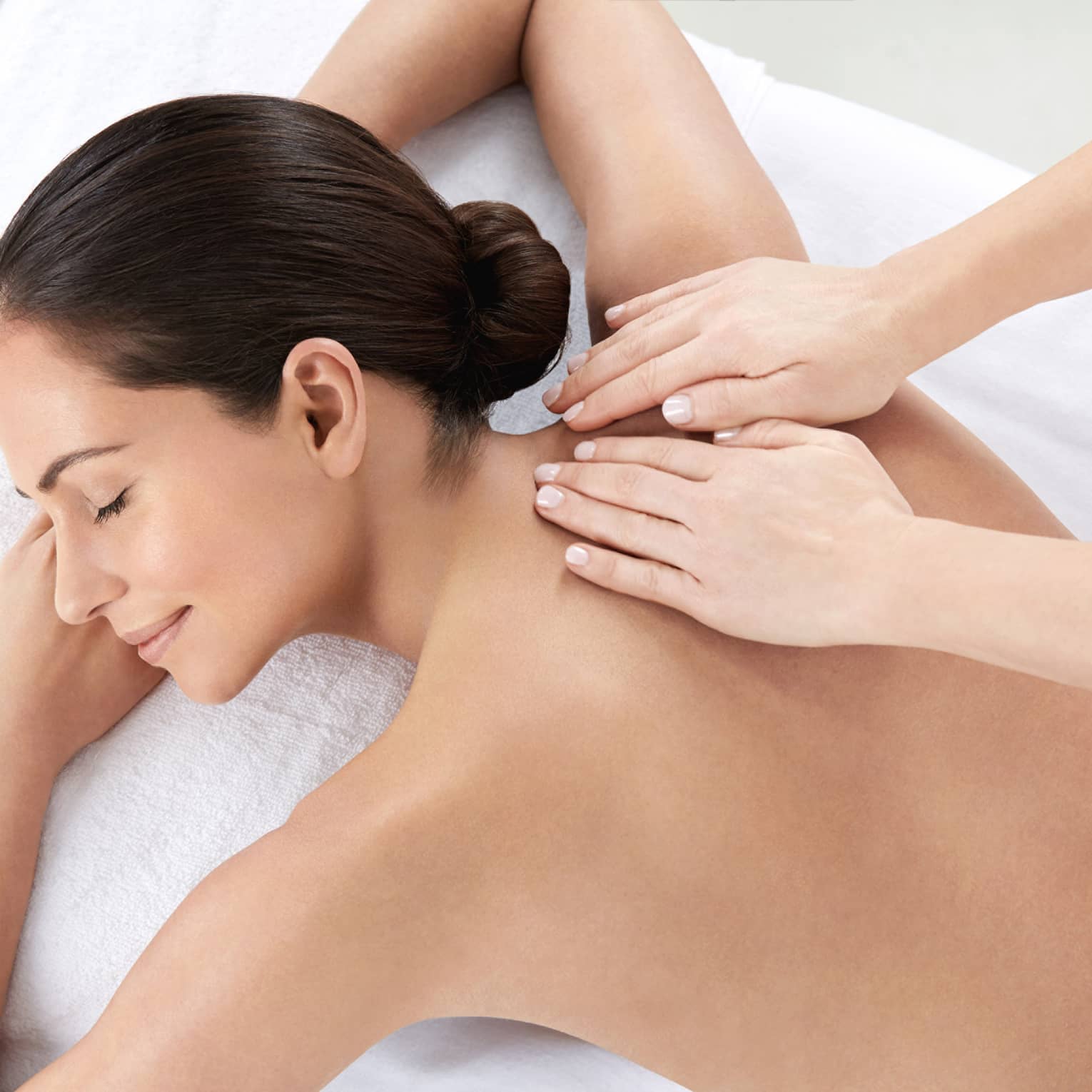 Woman smiles, lies on massage table as hands massage bare shoulders