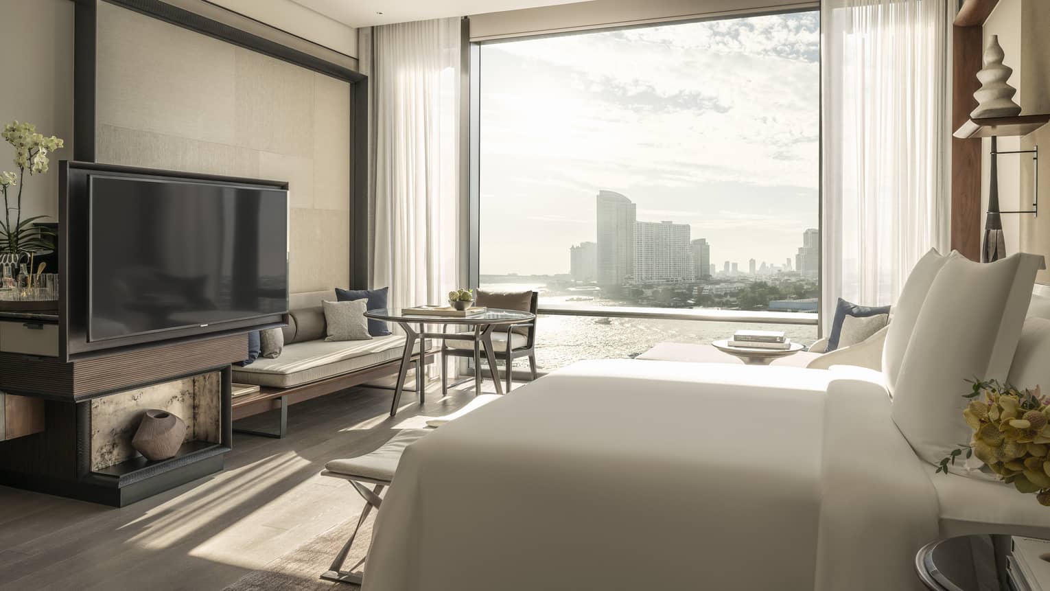 Guest room at Four Seasons Hotel Bangkok, with king bed, TV, sitting bench and view of river