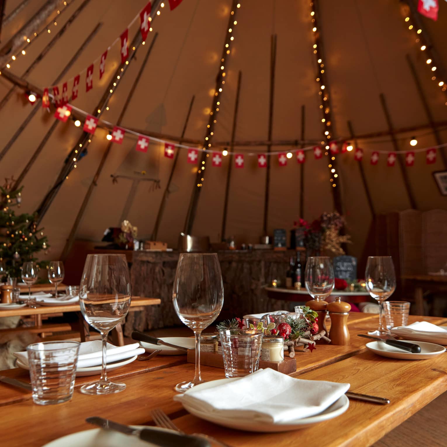 Holiday-decorated yurt with set wooden tables and string lights
