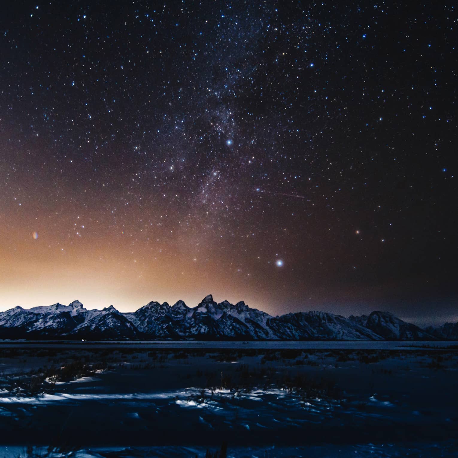 silhouette of mountains and solar flare across the starry night sky in winter