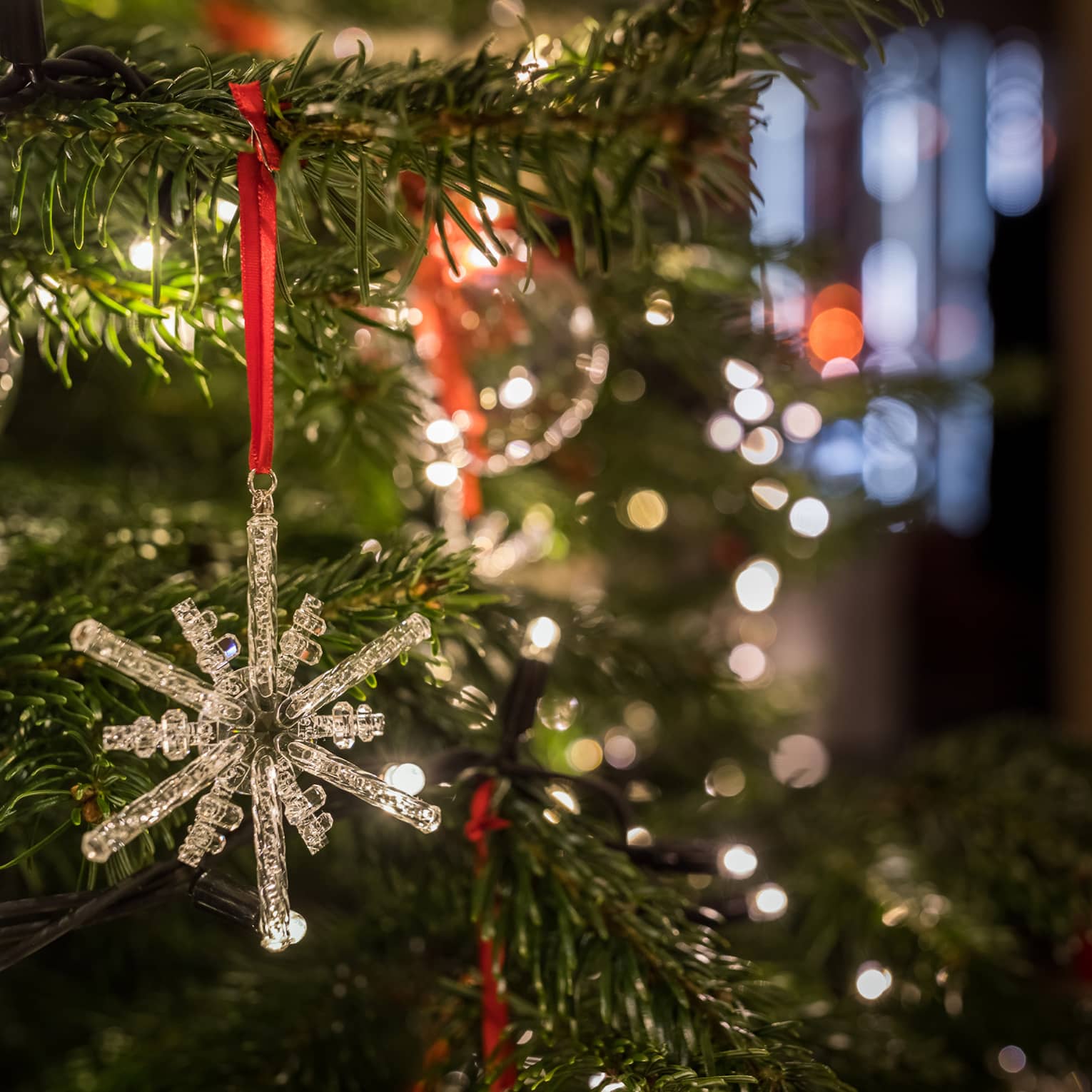 Close-up of a crystal snowflake ornament hanging on a Christmas tree with festive lights in the background