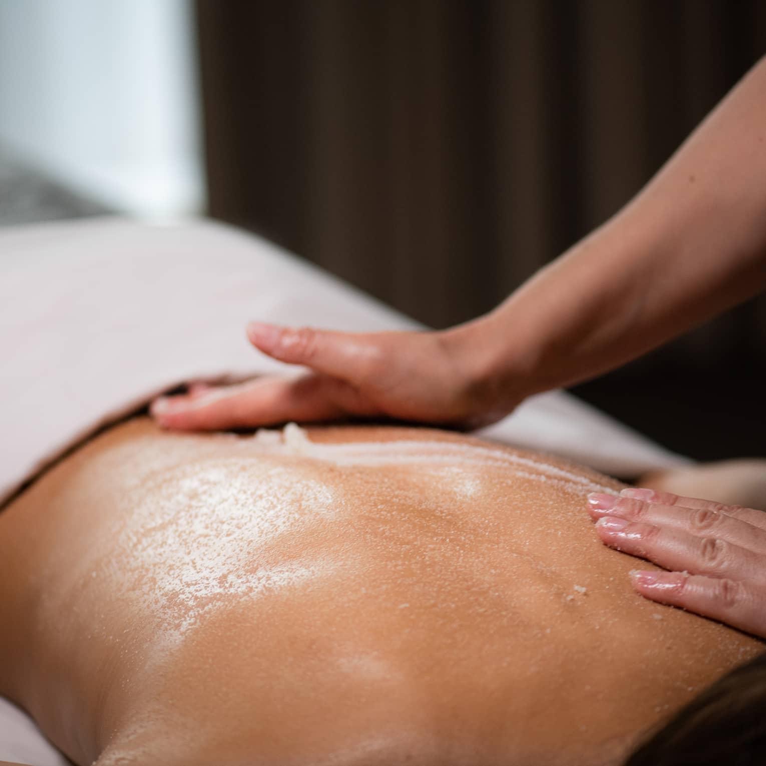 A masseuse spreads a cream across a woman's back as she lies on a massage table.
