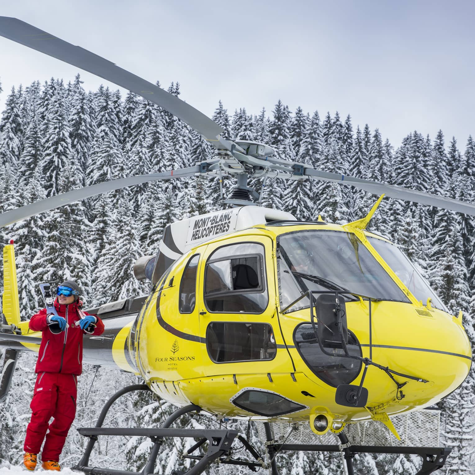 A yellow helicopter rests atop a snow covered mountain in Megeve