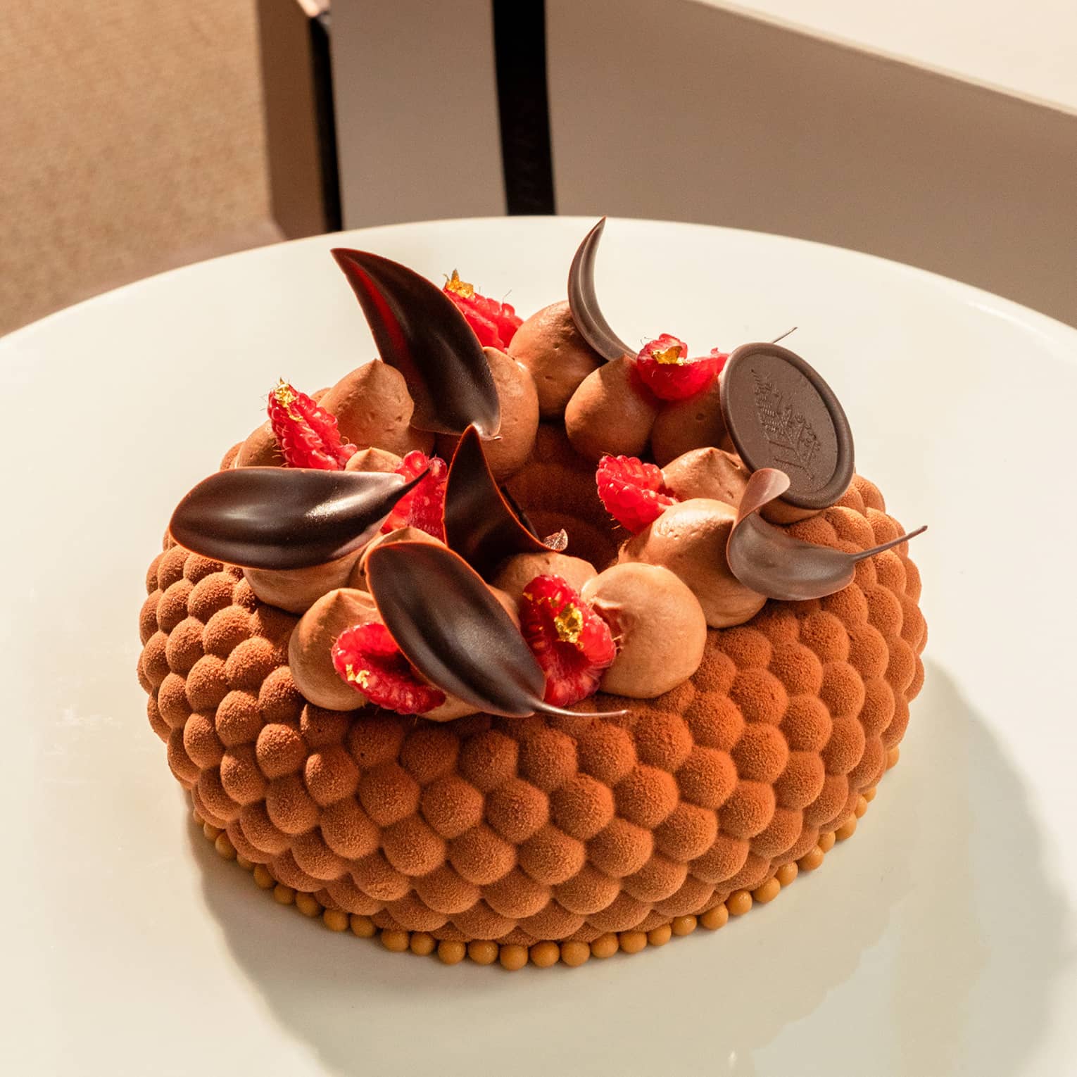 Chocolate gâteau topped with chocolate leaves, sliced raspberries and dollops of chocolate icing