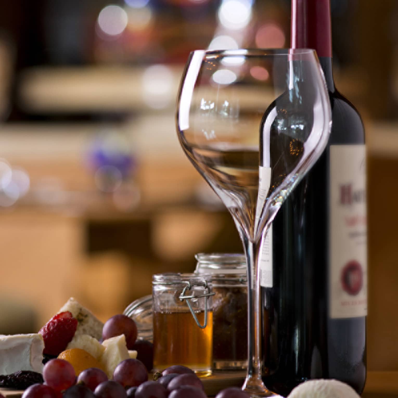 Large empty wine glass next to bottle of red wine, fresh grapes and cheese on counter