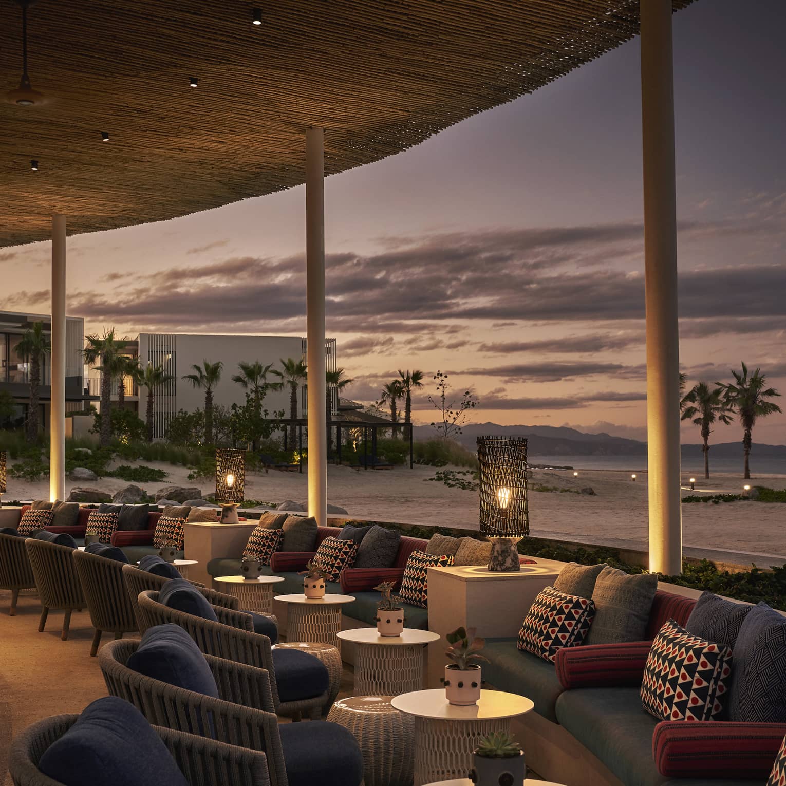 Dimly lit Casa de Brasa lounge area overlooking beach with palm trees at dusk