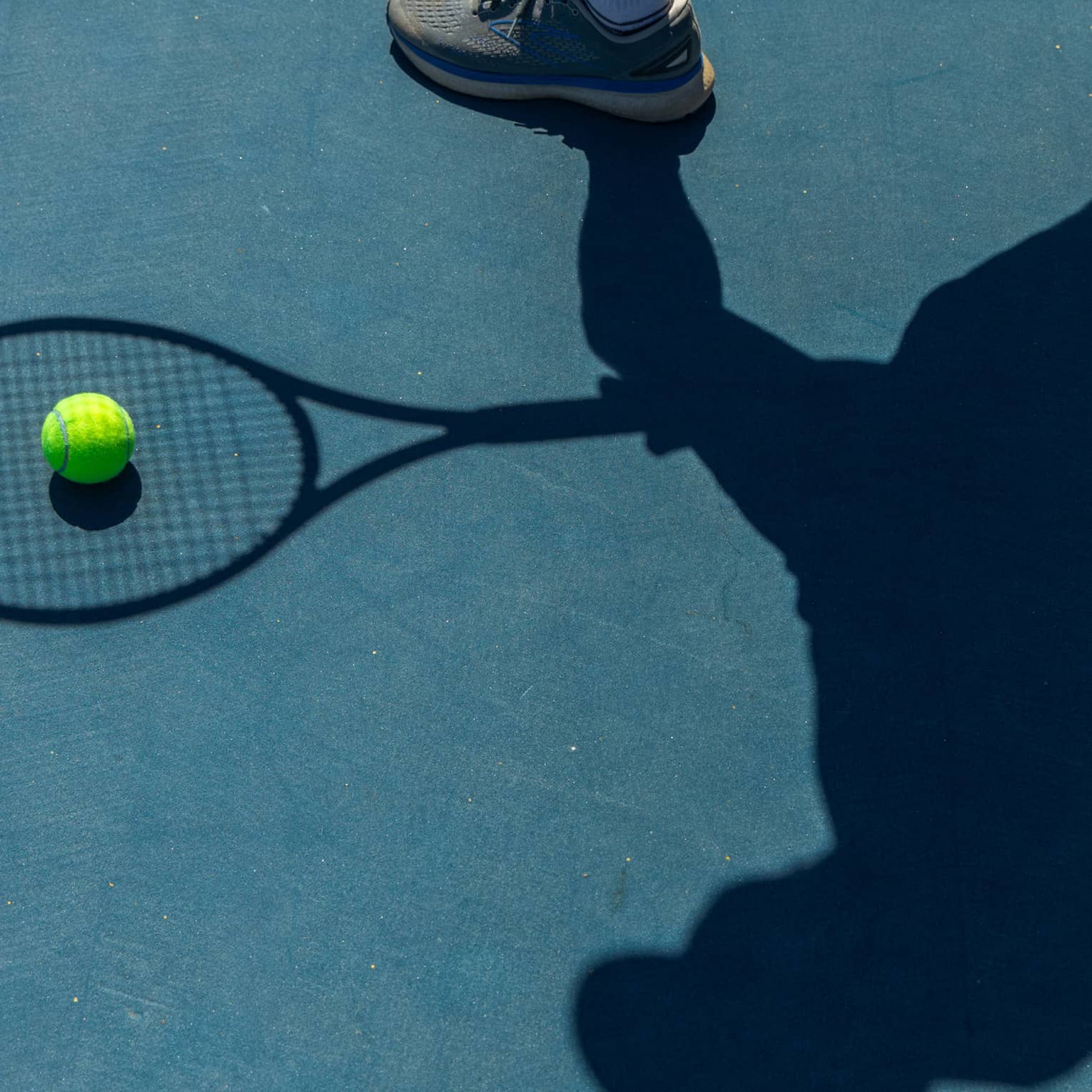 Shadow of a person and a tennis racquet, with a tennis ball in the middle of the racquet's shadow