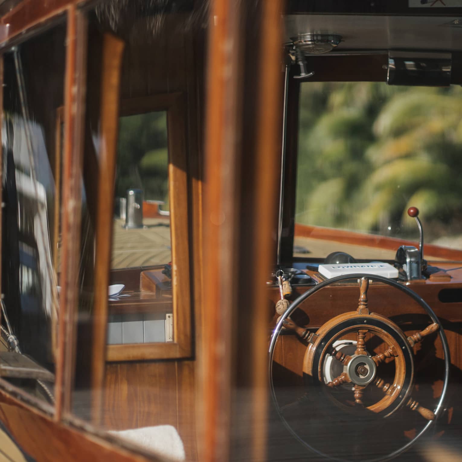 View from outside into a boat's cockpit cabin, both the boat's frame and the wheel partly made of rustic deep-brown wood.