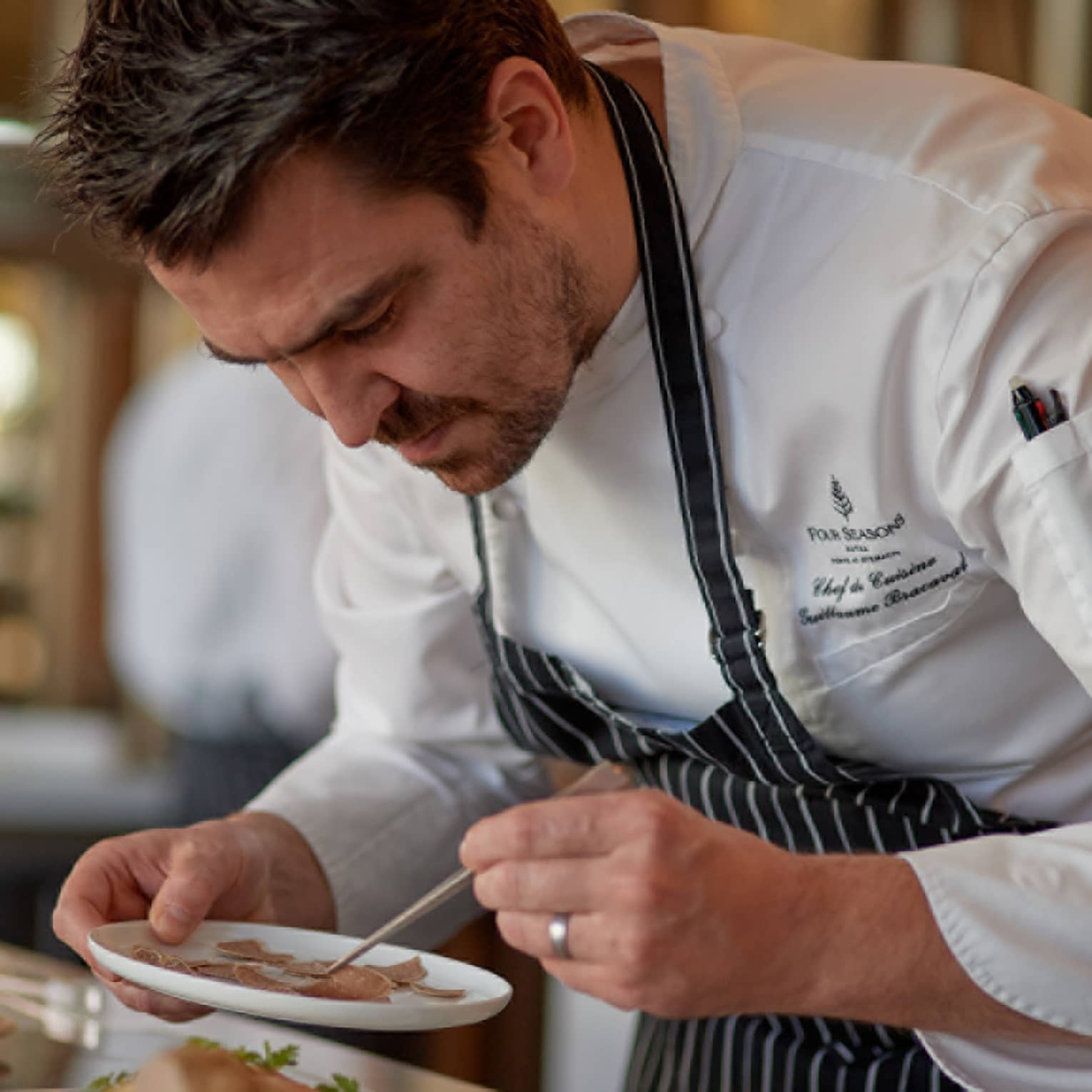 Four Seasons chef in striped apron carefully plating a dish in a kitchen