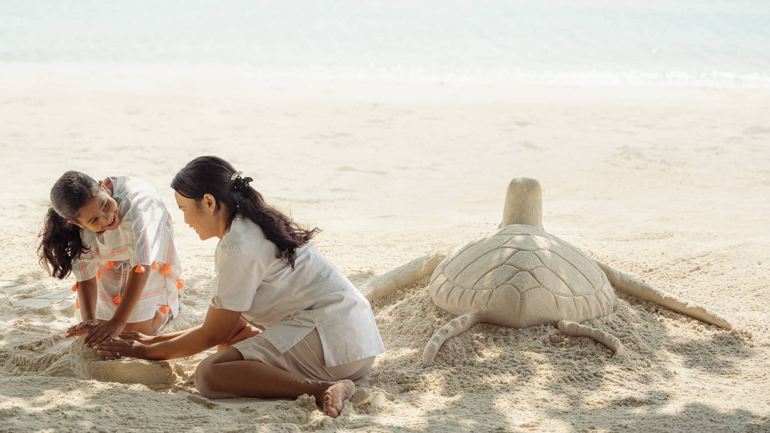 Young girl and dedicated attendant build a sea turtle out of sand at the water's edge