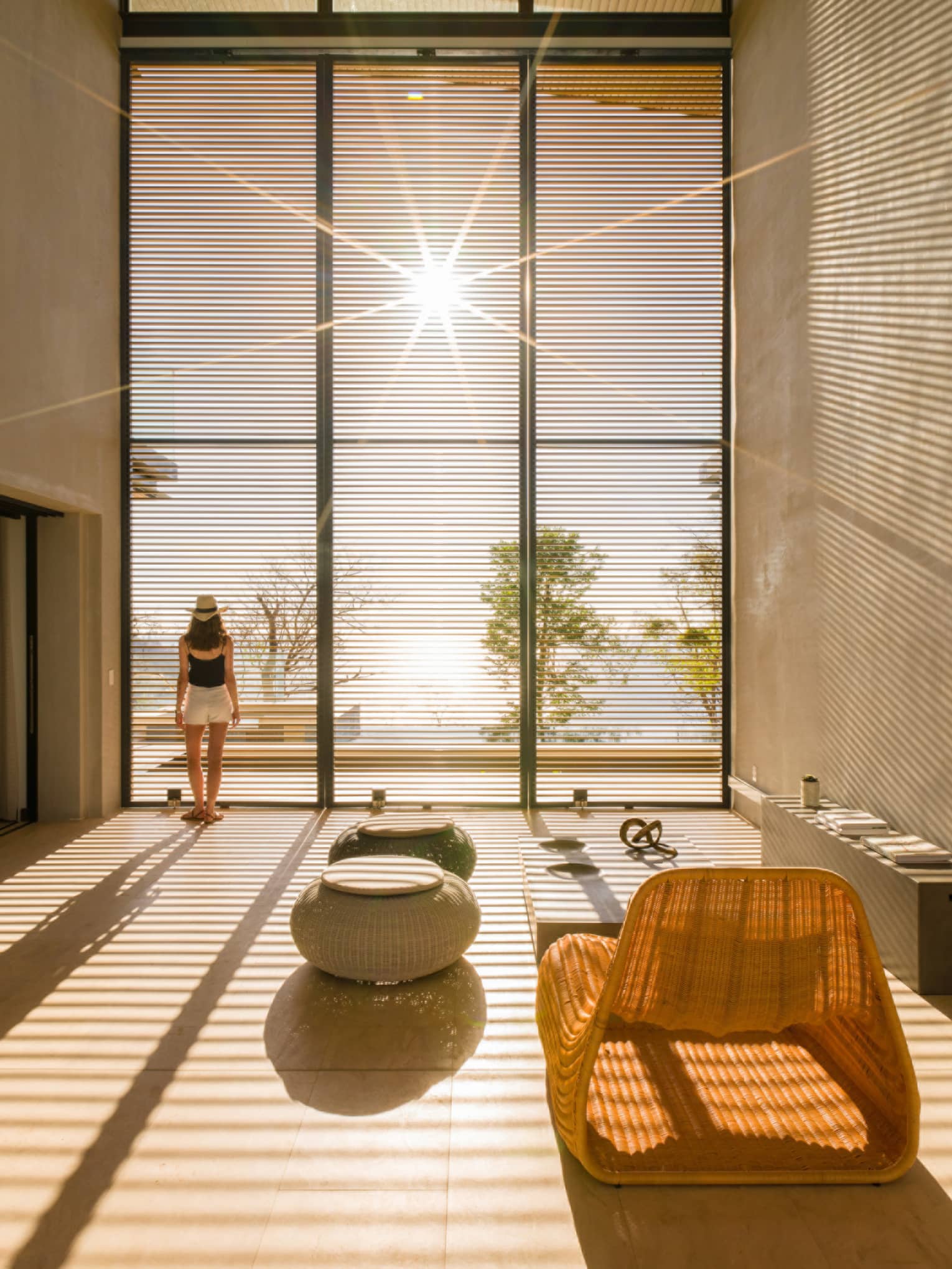 Woman stands by sunny floor to ceiling window in modern room