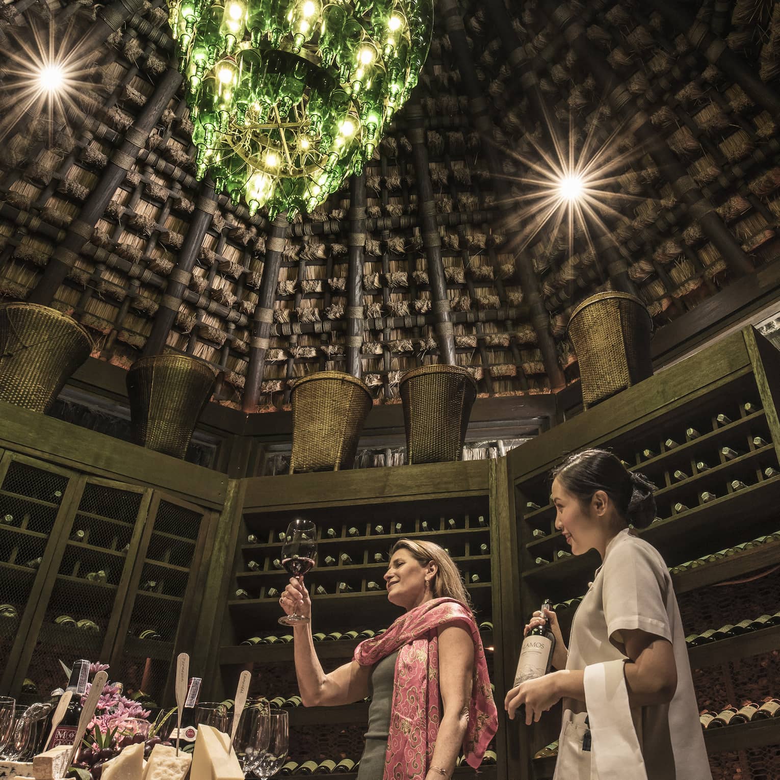 Two people in rustic wine cellar with a green bottle chandelier