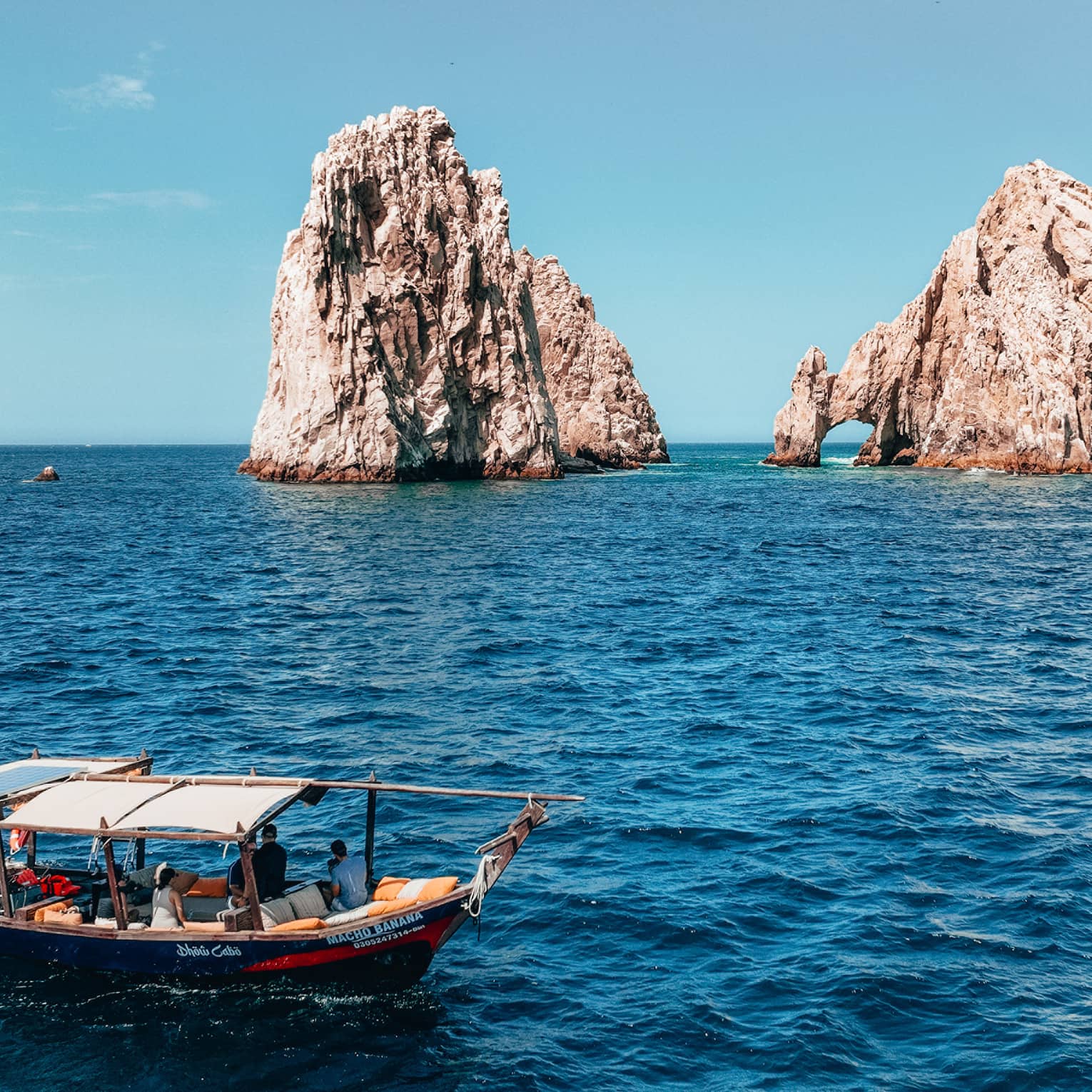 A canopied wooden tour boat in open water with tall craggy rock formations jutting out of the ocean in the background.