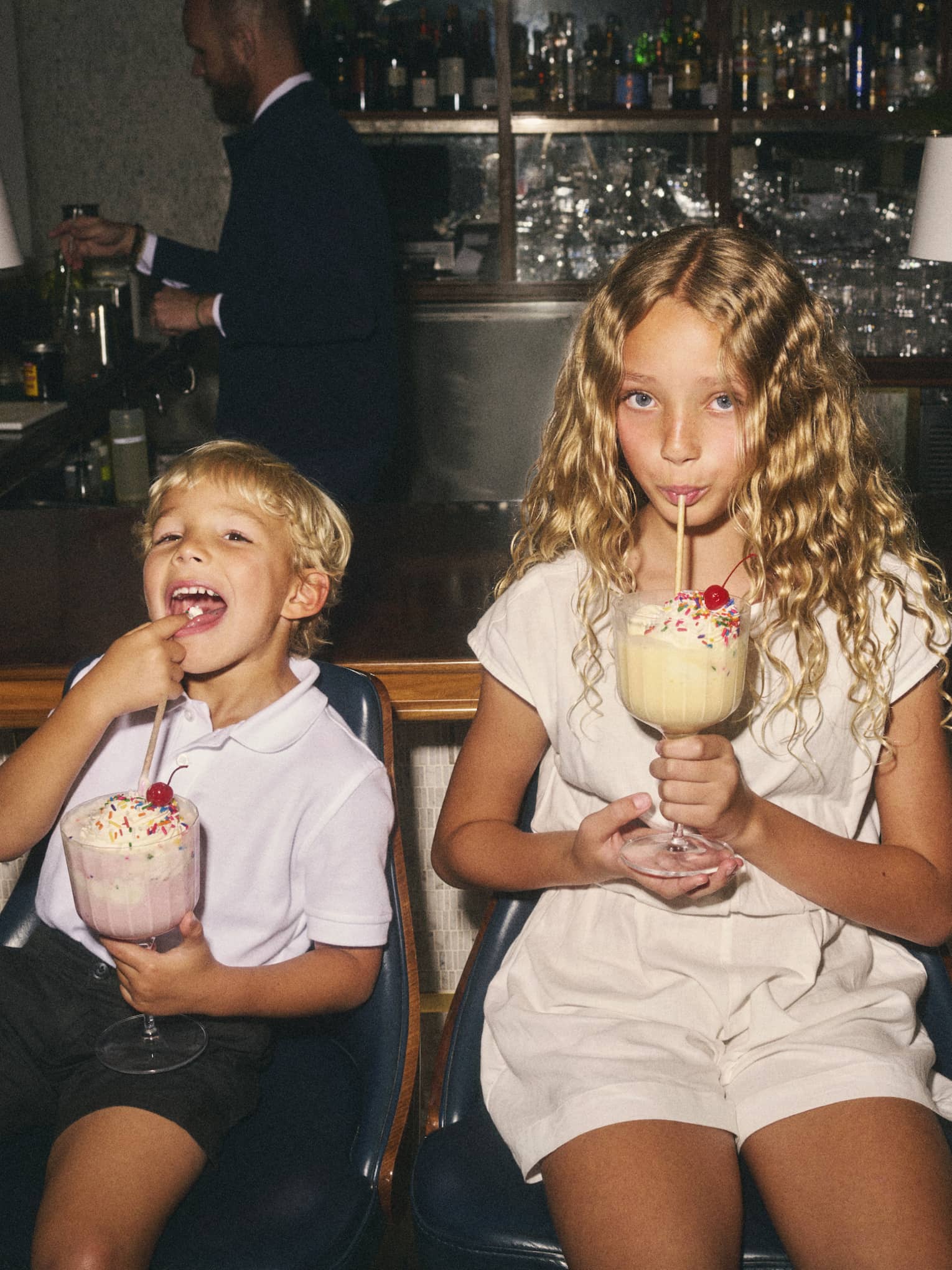 Two children sit on counter stools sipping on large milkshakes