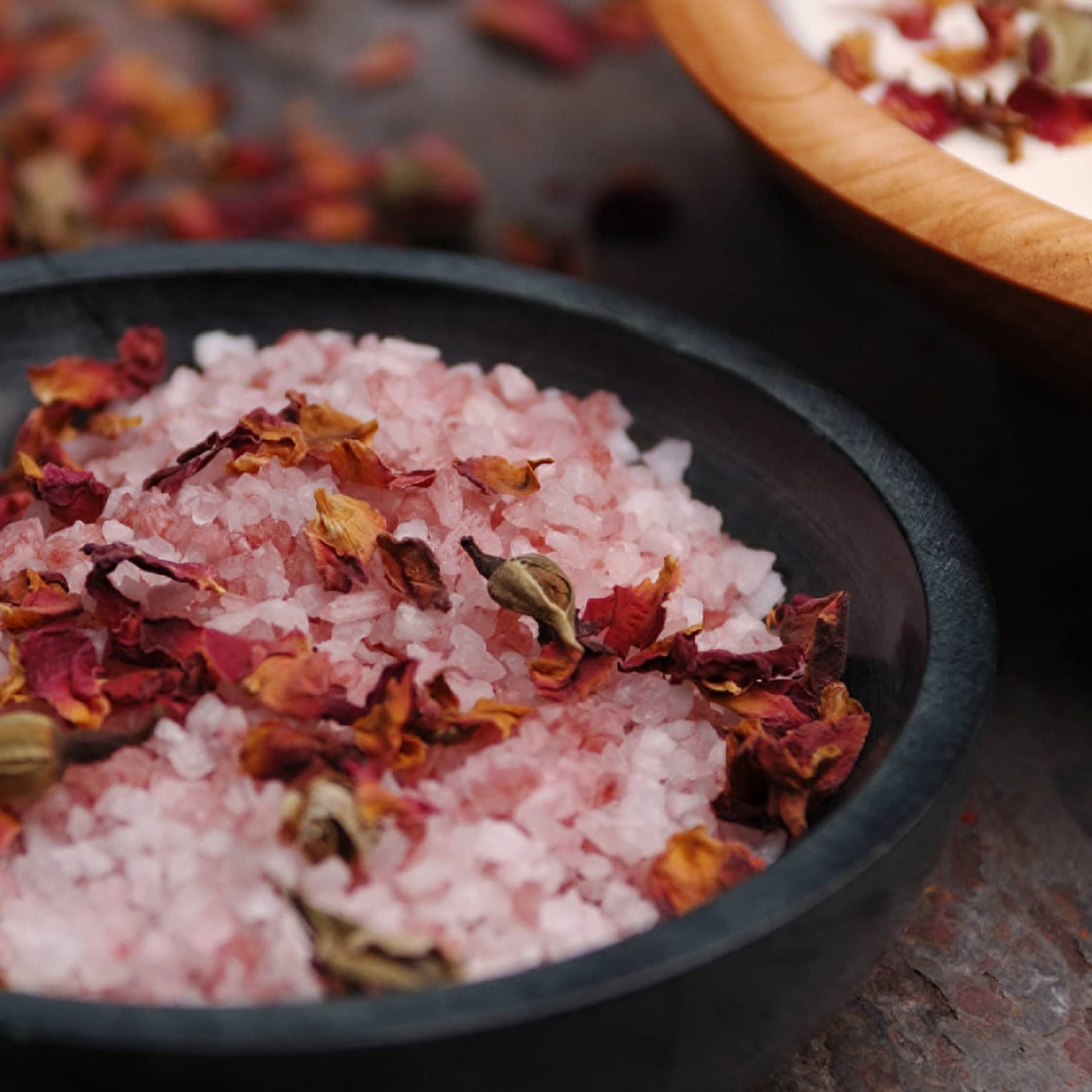 Pink crystals or salt and red flowers in a black bowl.