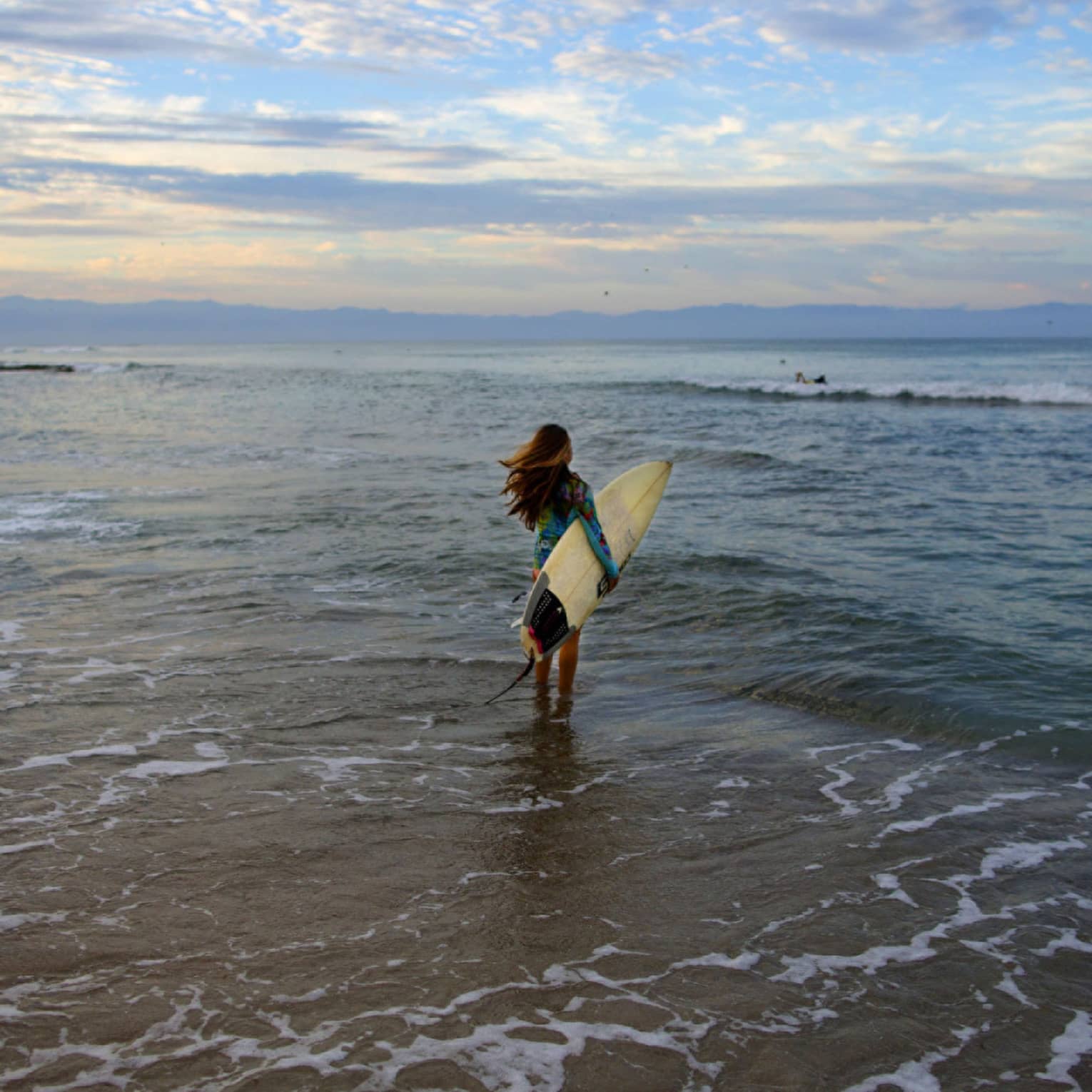 A woman holding a surfboard while walking towards ocean waves.