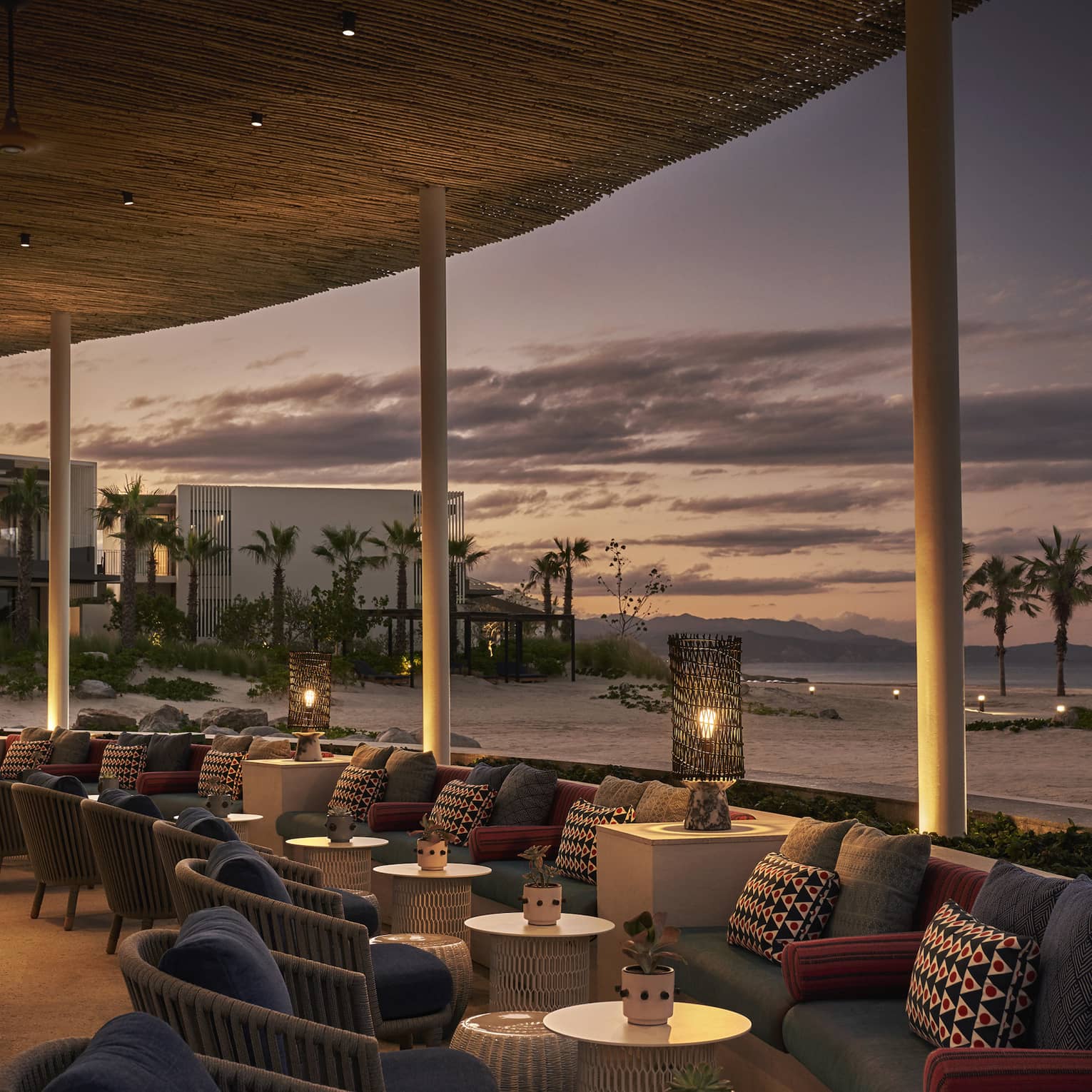 Dimly lit Casa de Brasa lounge area overlooking beach with palm trees at dusk